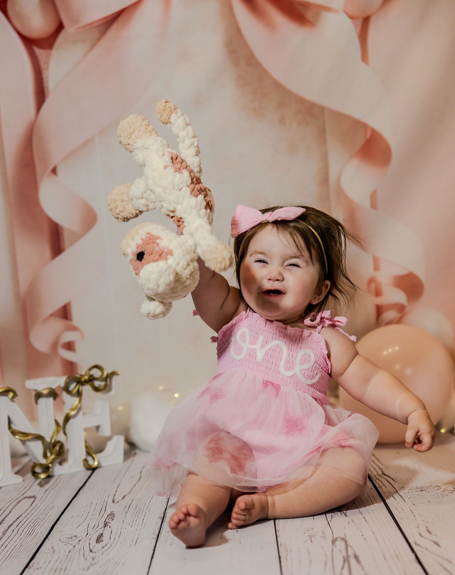 Baby in pink tutu dress celebrating against a peachy pink balloon backdrop.