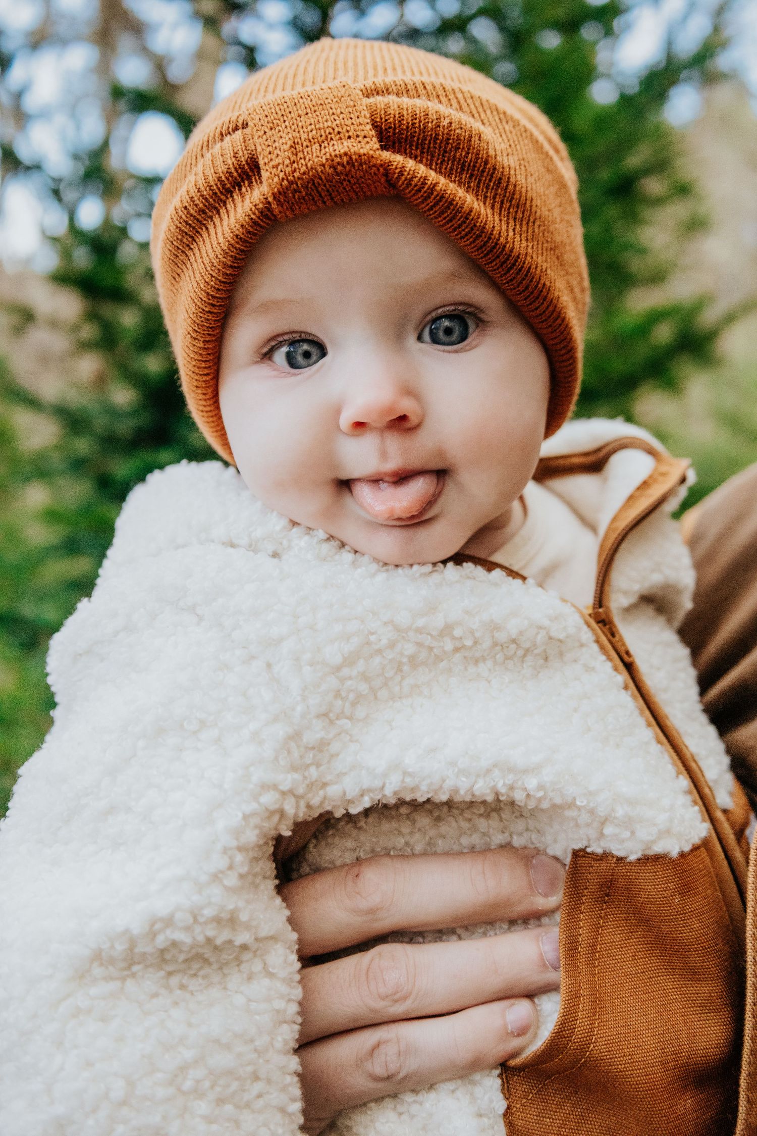 Baby wearing orange beanie and white sherpa outfit smiling at camera in outdoor setting.