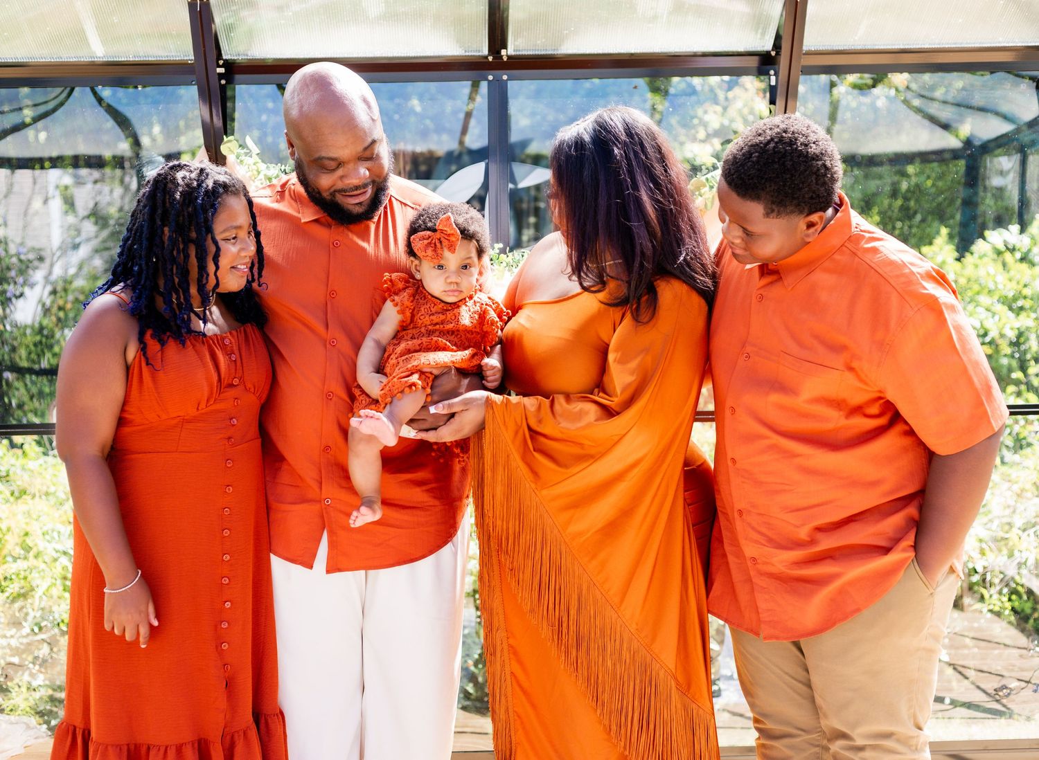 Group wearing coordinated orange outfits poses together in casual outdoor setting.