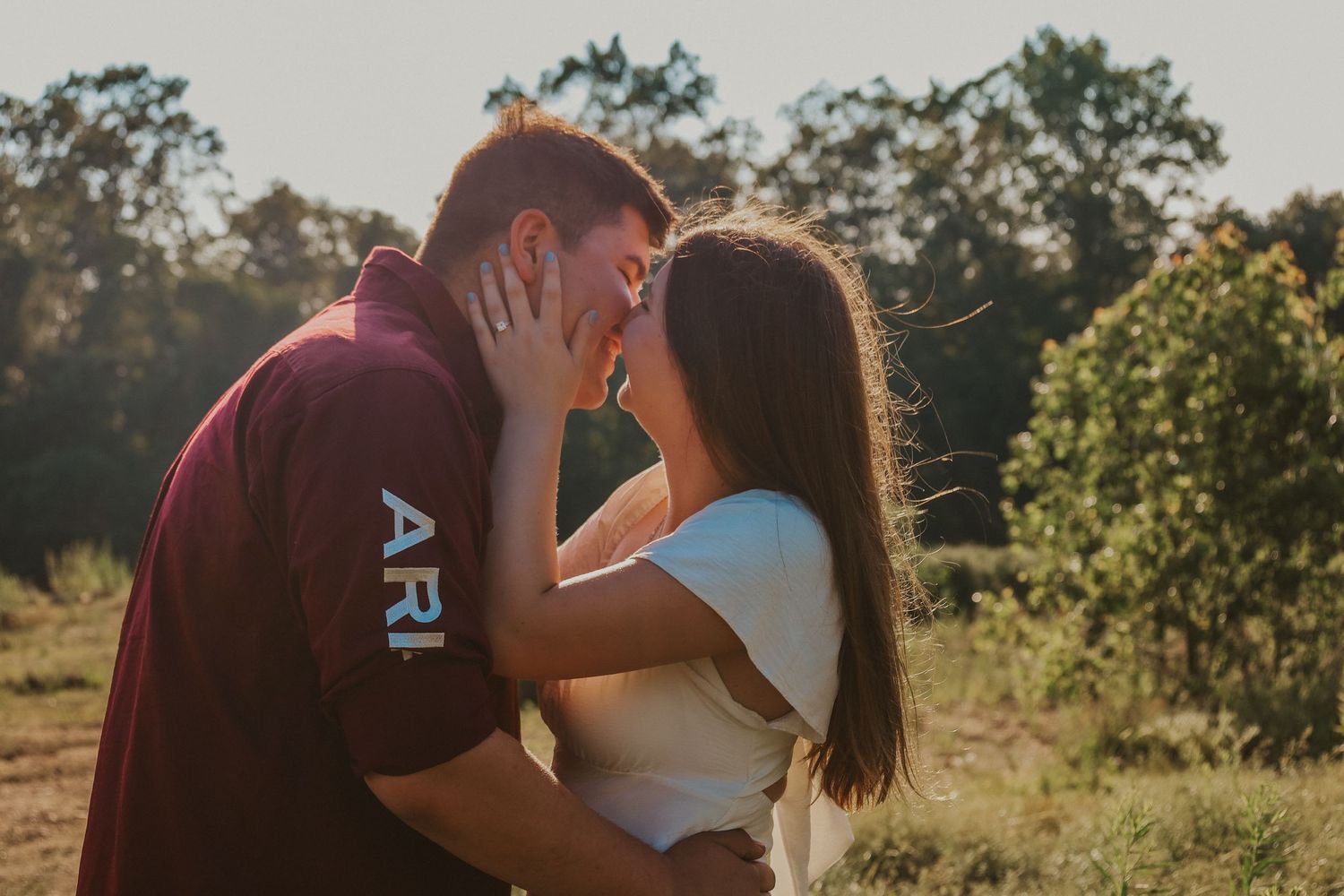 A romantic couple embraces in golden sunlight during an outdoor photo session.