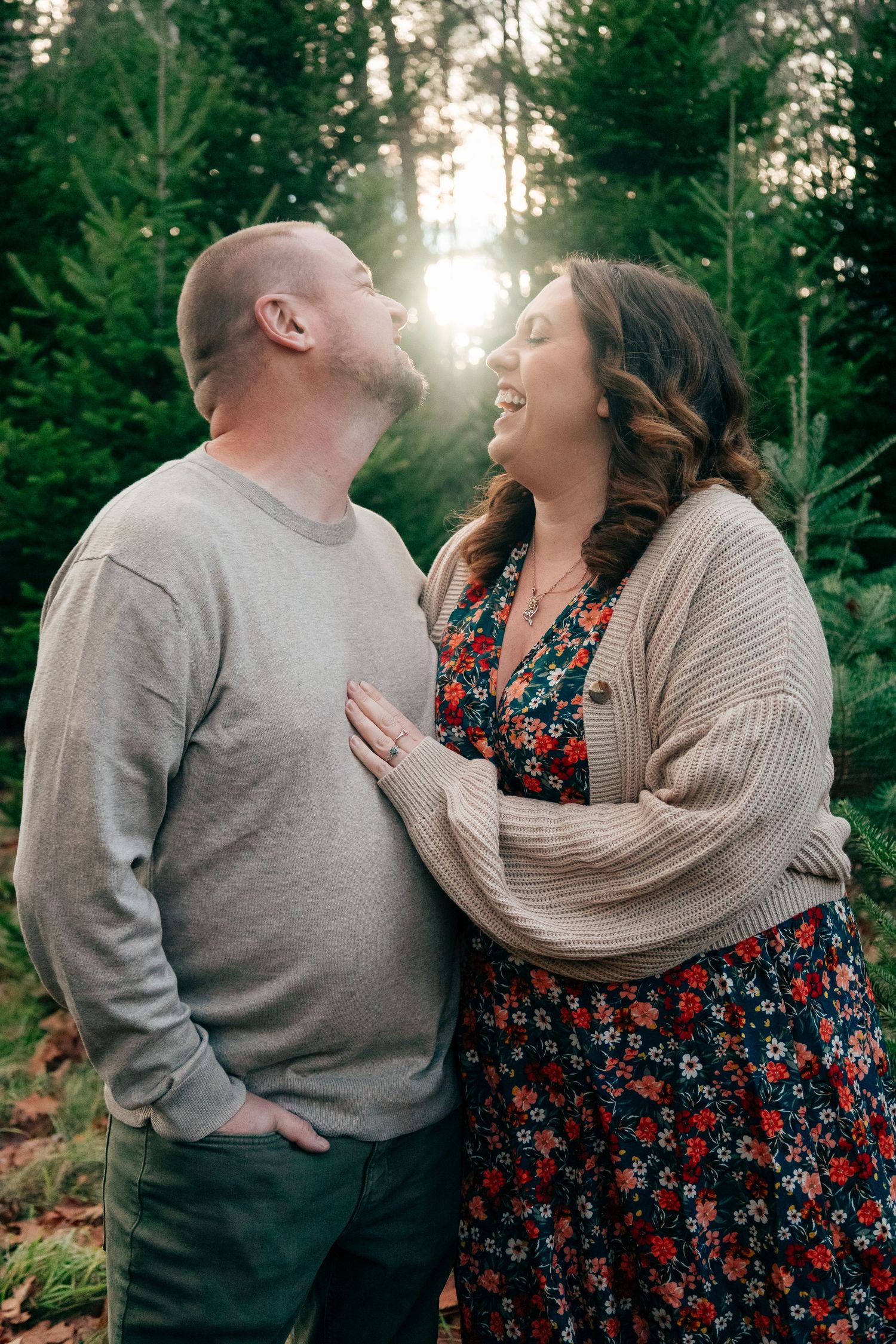 A couple shares joyful laughter during a forest photoshoot at sunset.
