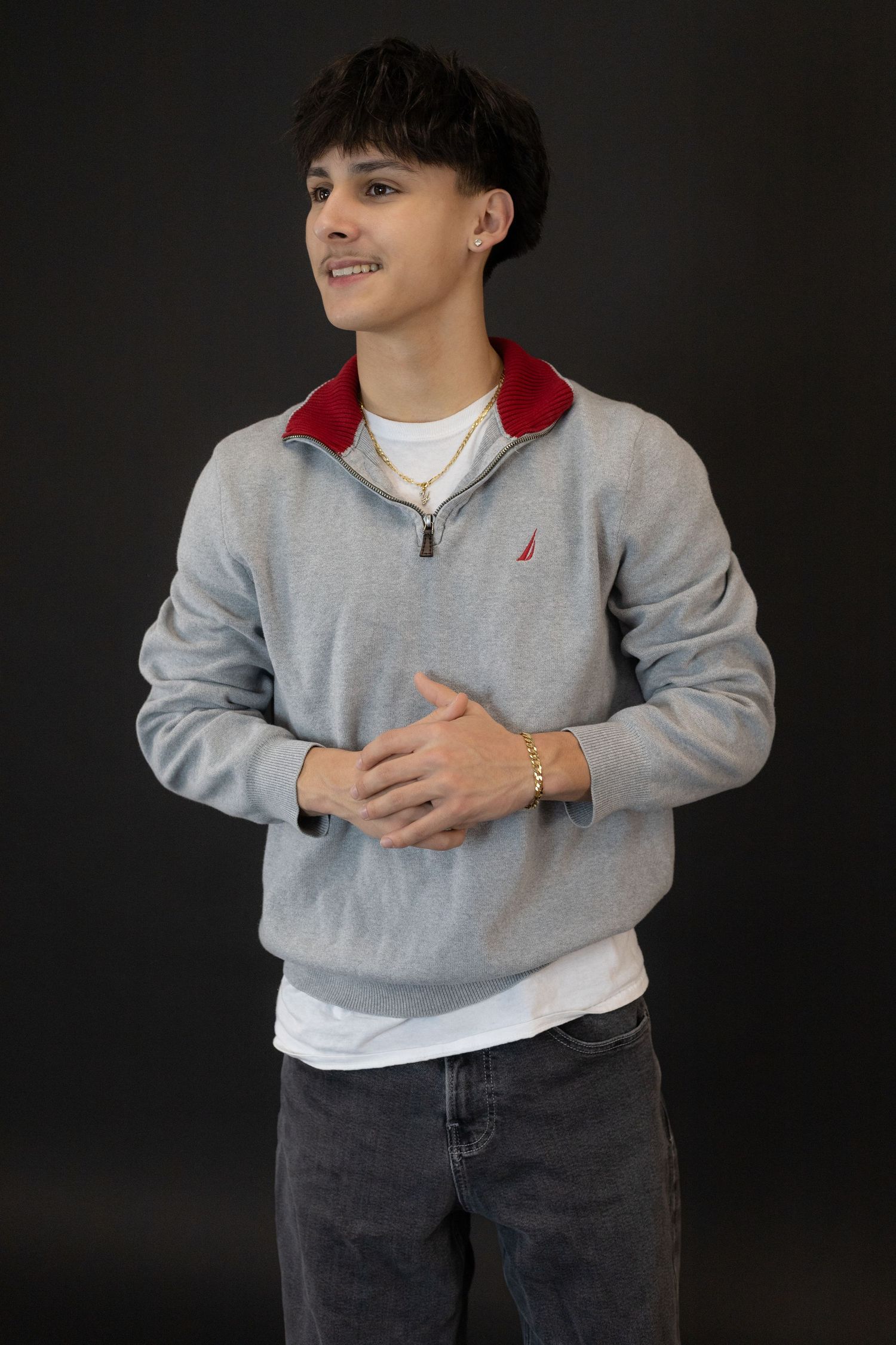 Teen boy in gray Nautica quarter-zip sweatshirt with red collar posing against dark background.