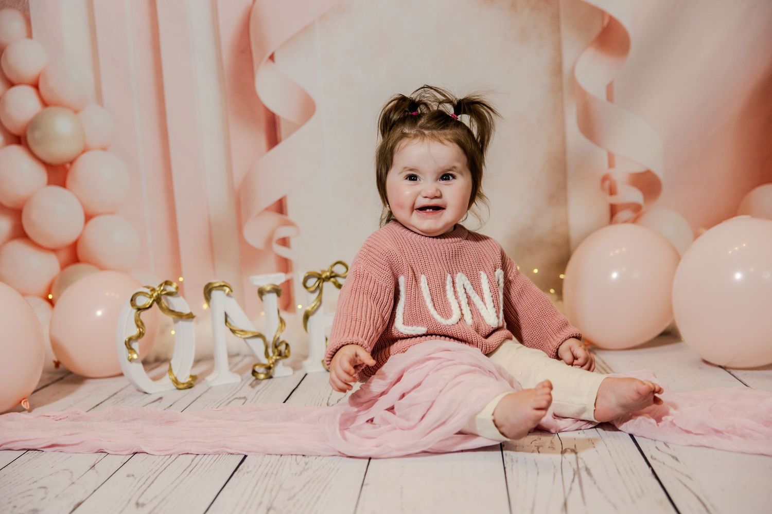 Baby photoshoot setup with pink balloons and white wooden floor decorations.