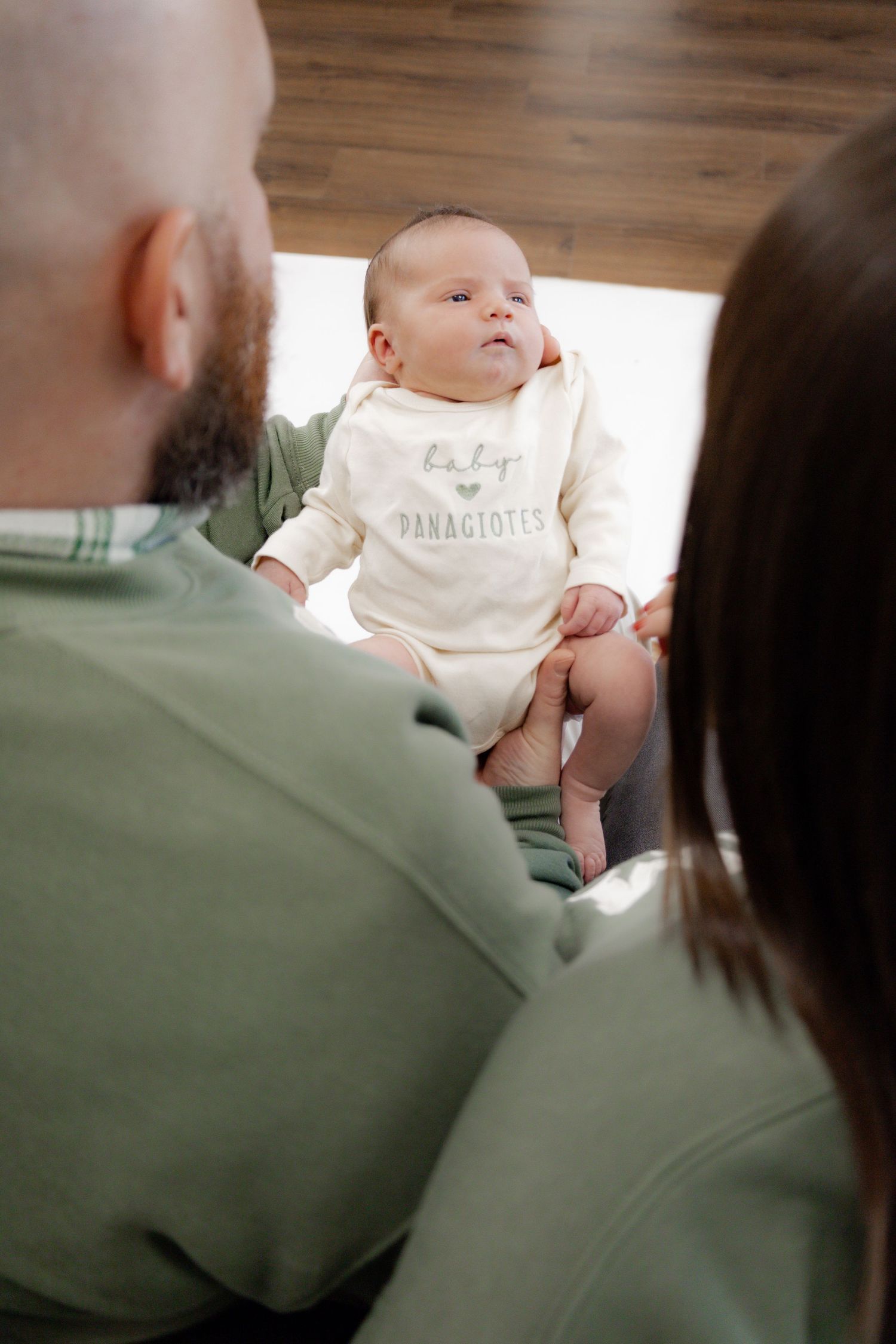 Baby wearing a white onesie being held on a green couch in natural lighting.