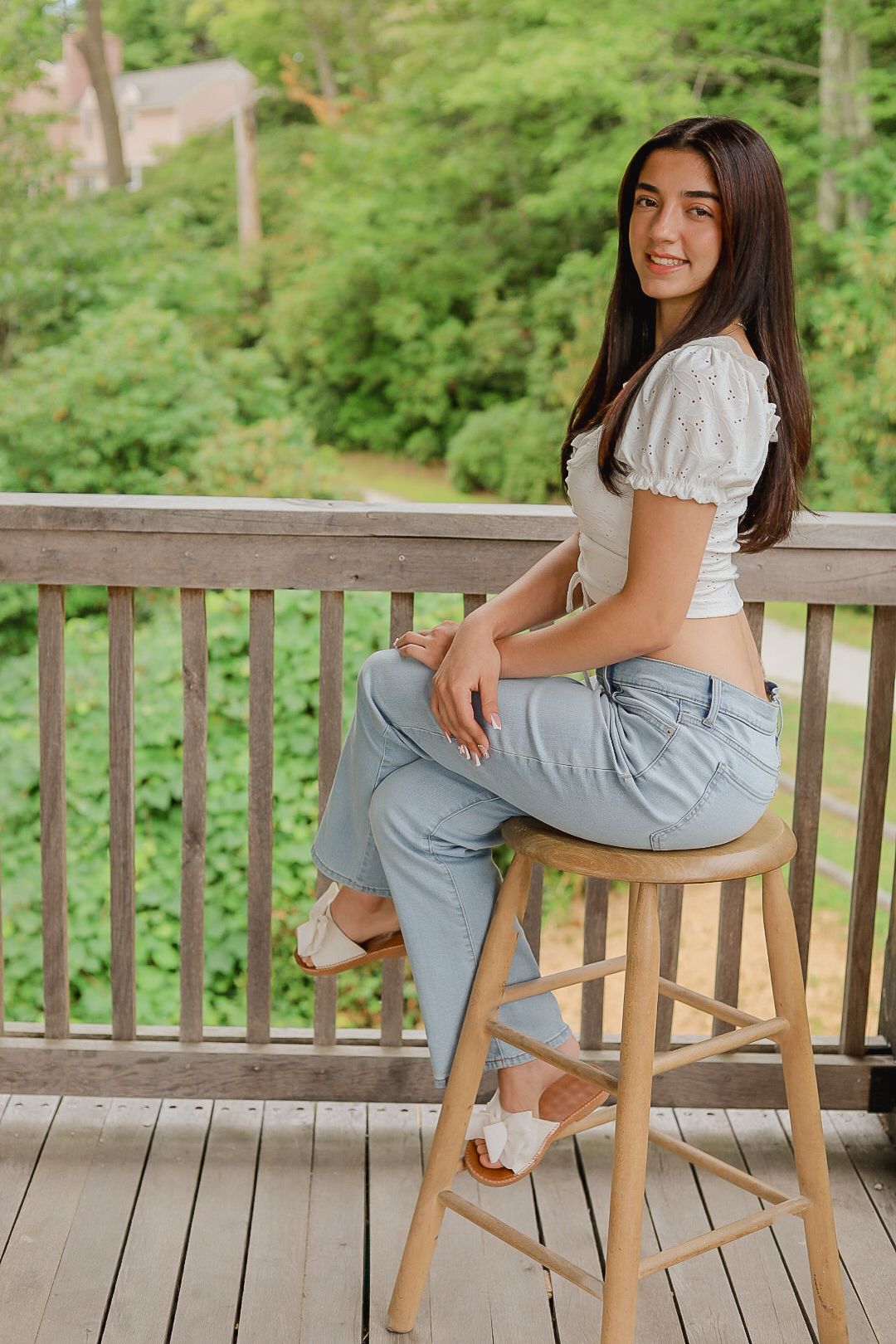 Someone relaxes on a wooden chair on a deck overlooking lush green forest.