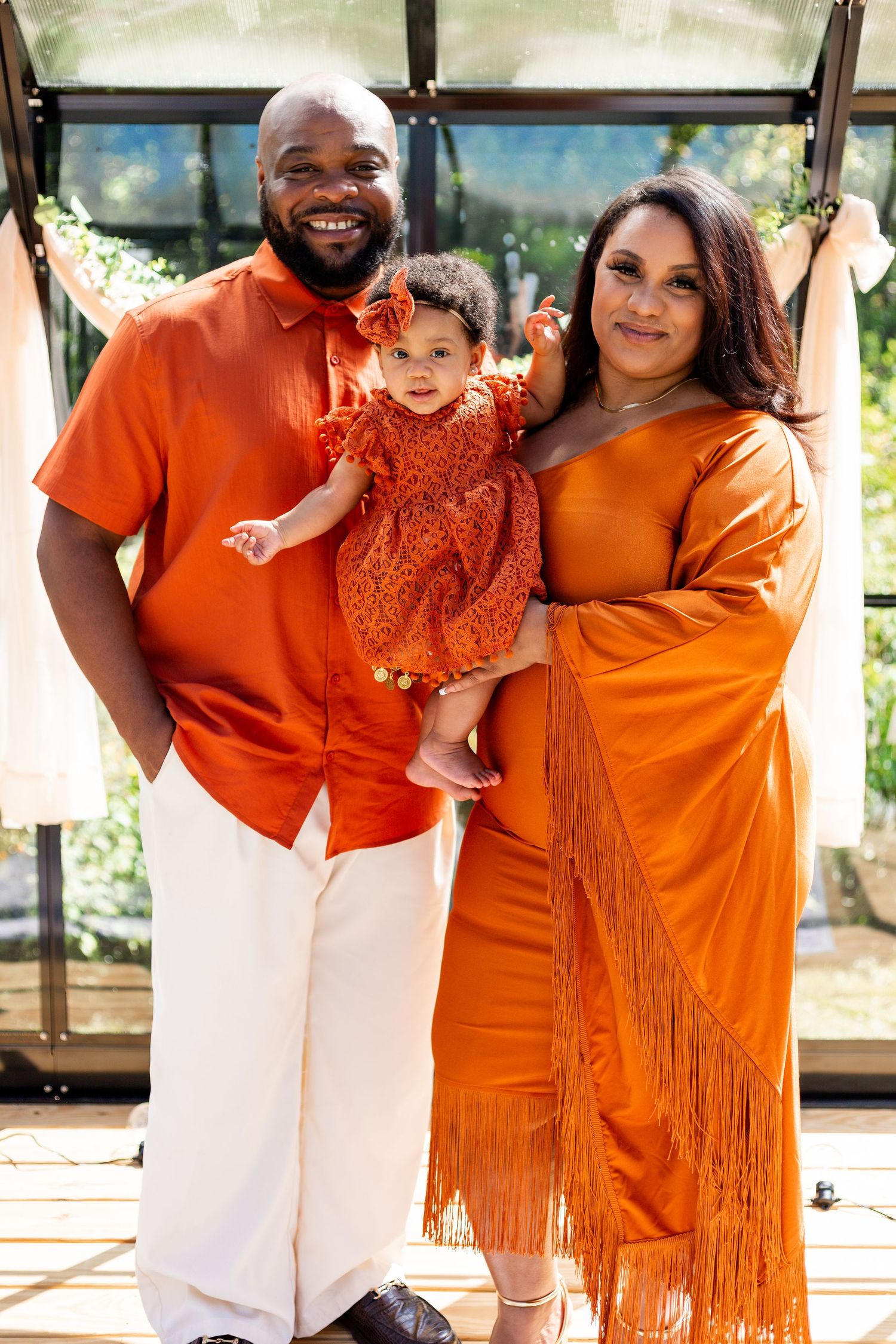 A family wearing coordinated orange outfits poses together in a greenhouse setting.