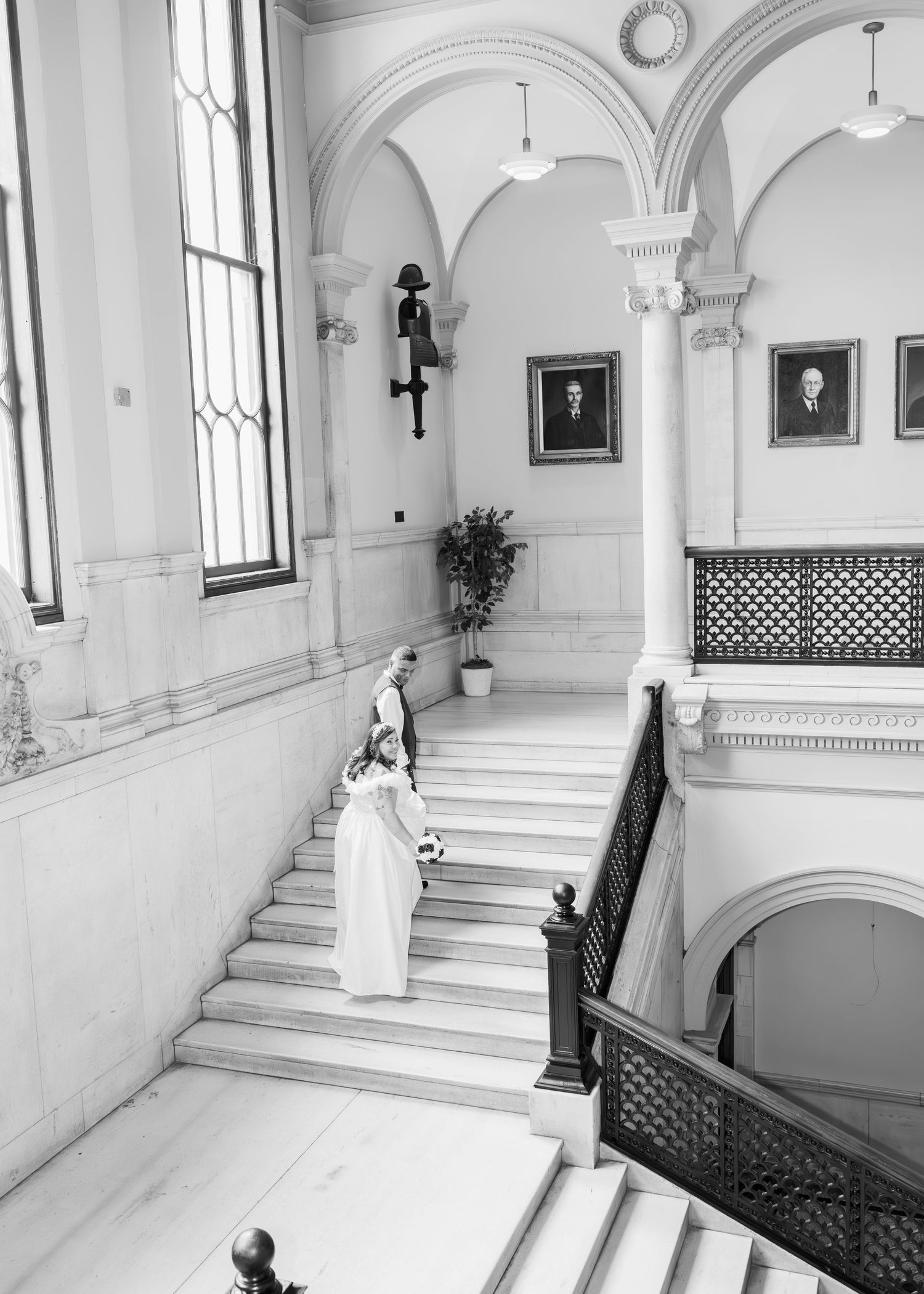 Black and white photo of bride ascending grand marble staircase in a historic building.
