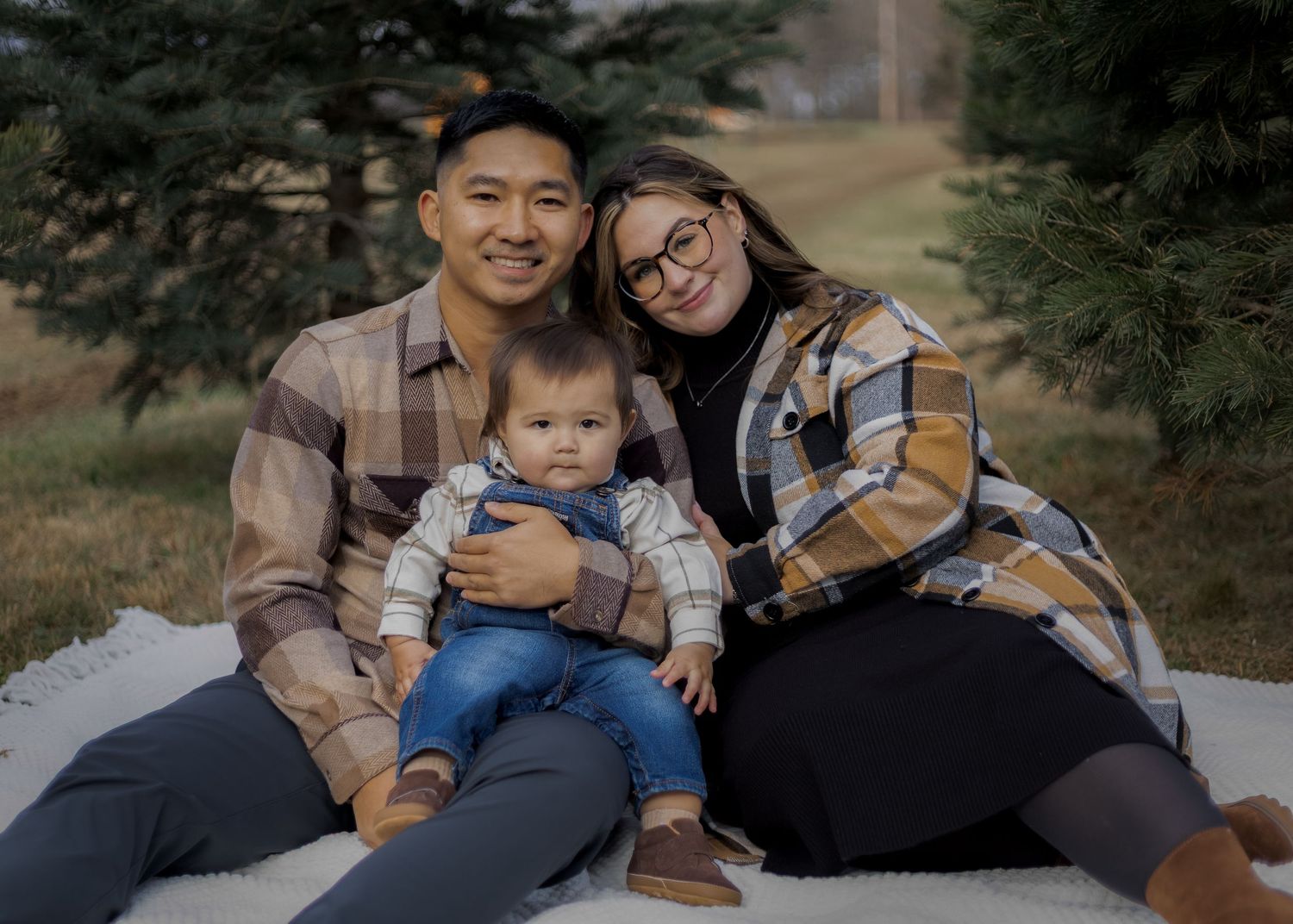 A family relaxes together on a blanket during an outdoor photoshoot among pine trees.