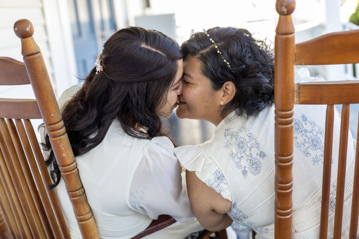 Two people share an intimate moment while sitting in wooden rocking chairs.