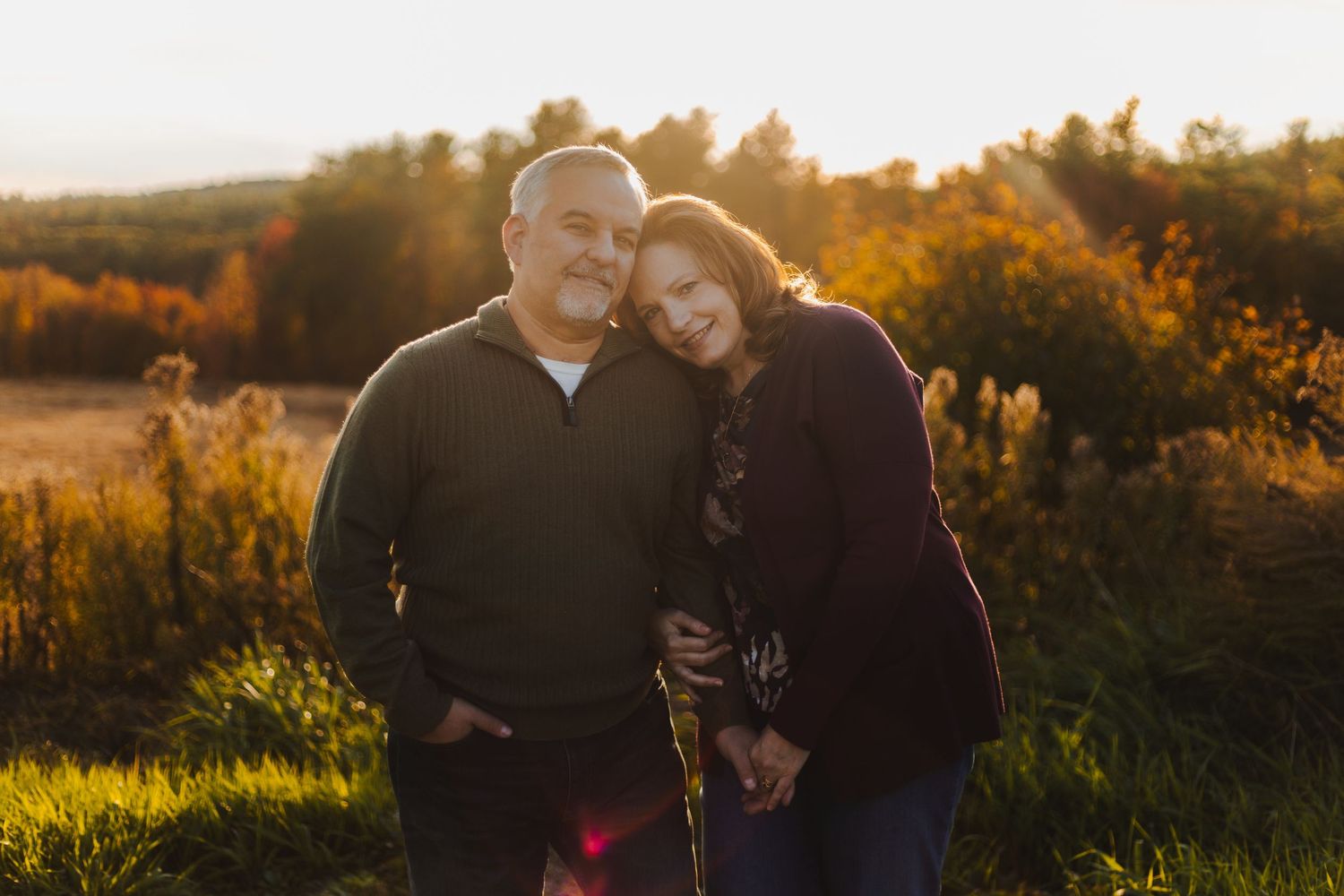Affectionate couple embracing in golden sunset light with autumn foliage in background.
