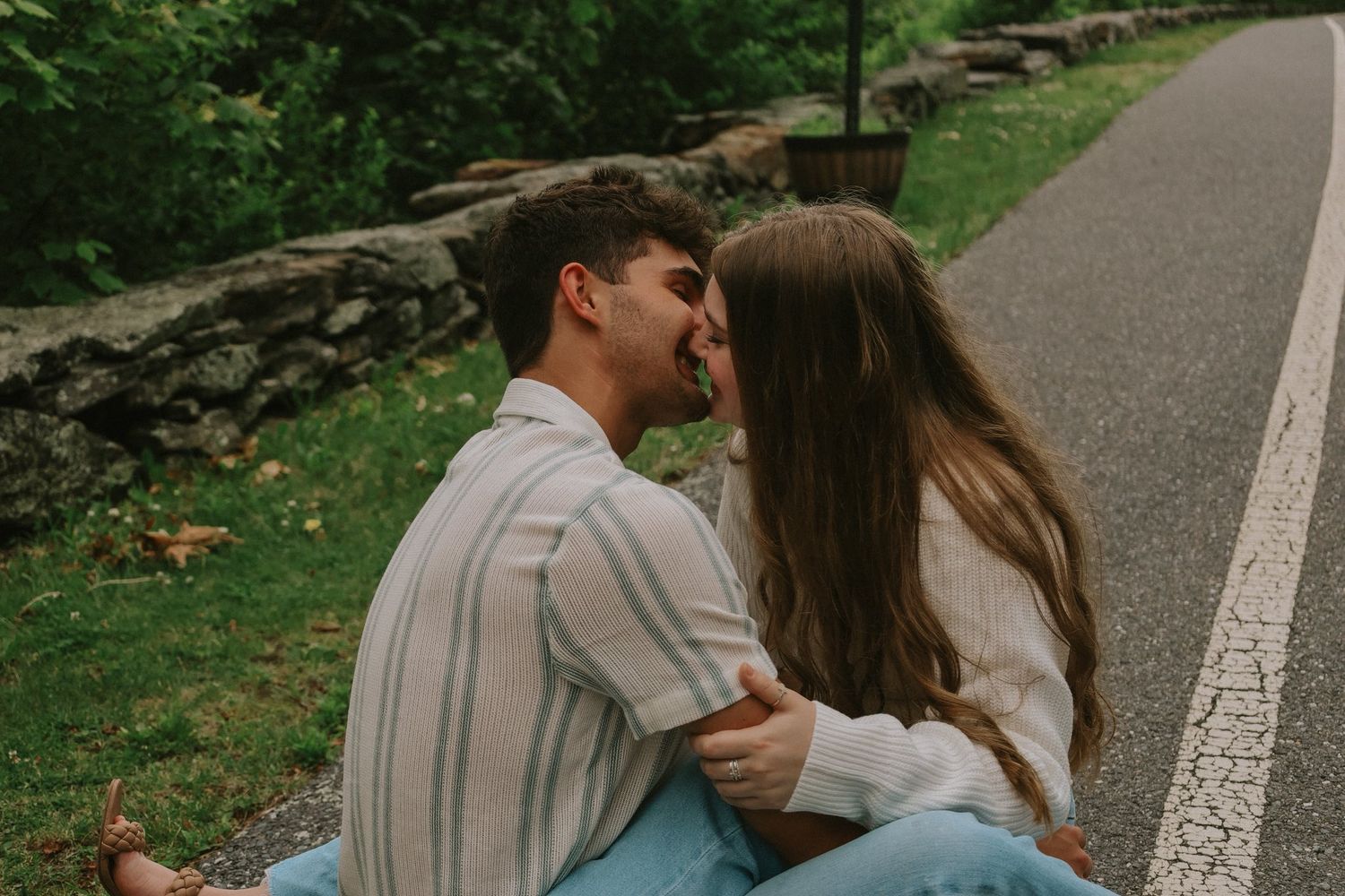 A romantic couple sharing an intimate moment while sitting together on a stone wall path.