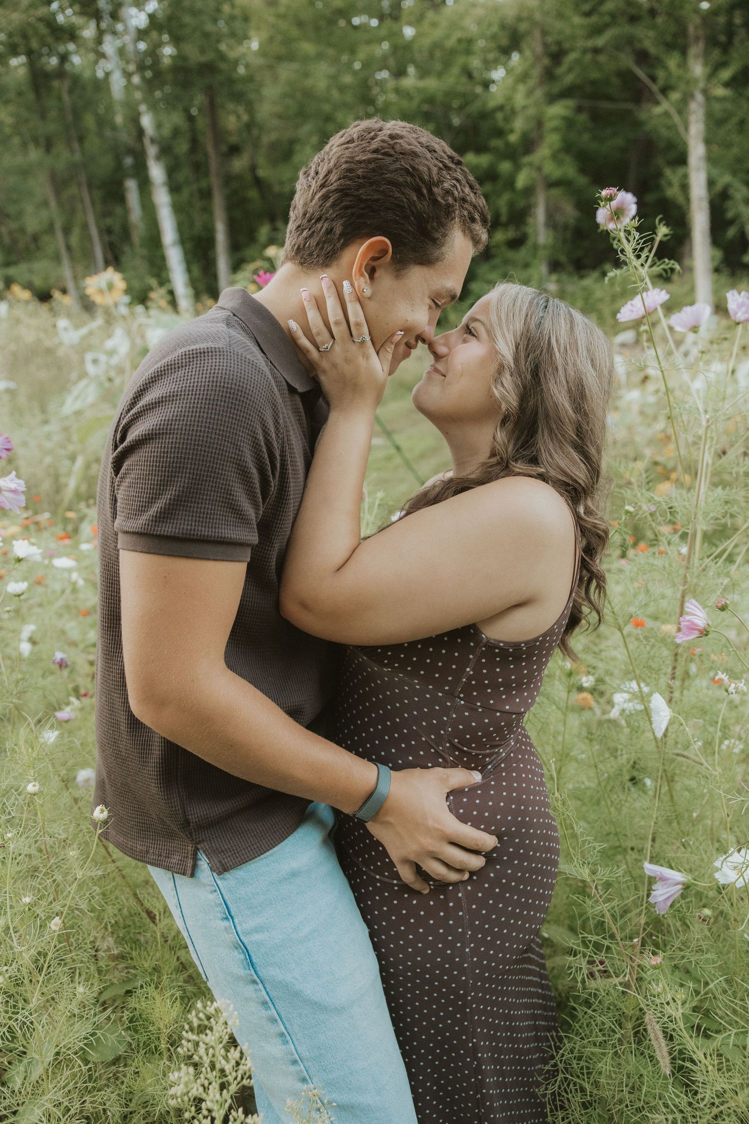 A couple shares a romantic almost-kiss moment in a wildflower meadow, the woman in a polka dot dress touching his face.