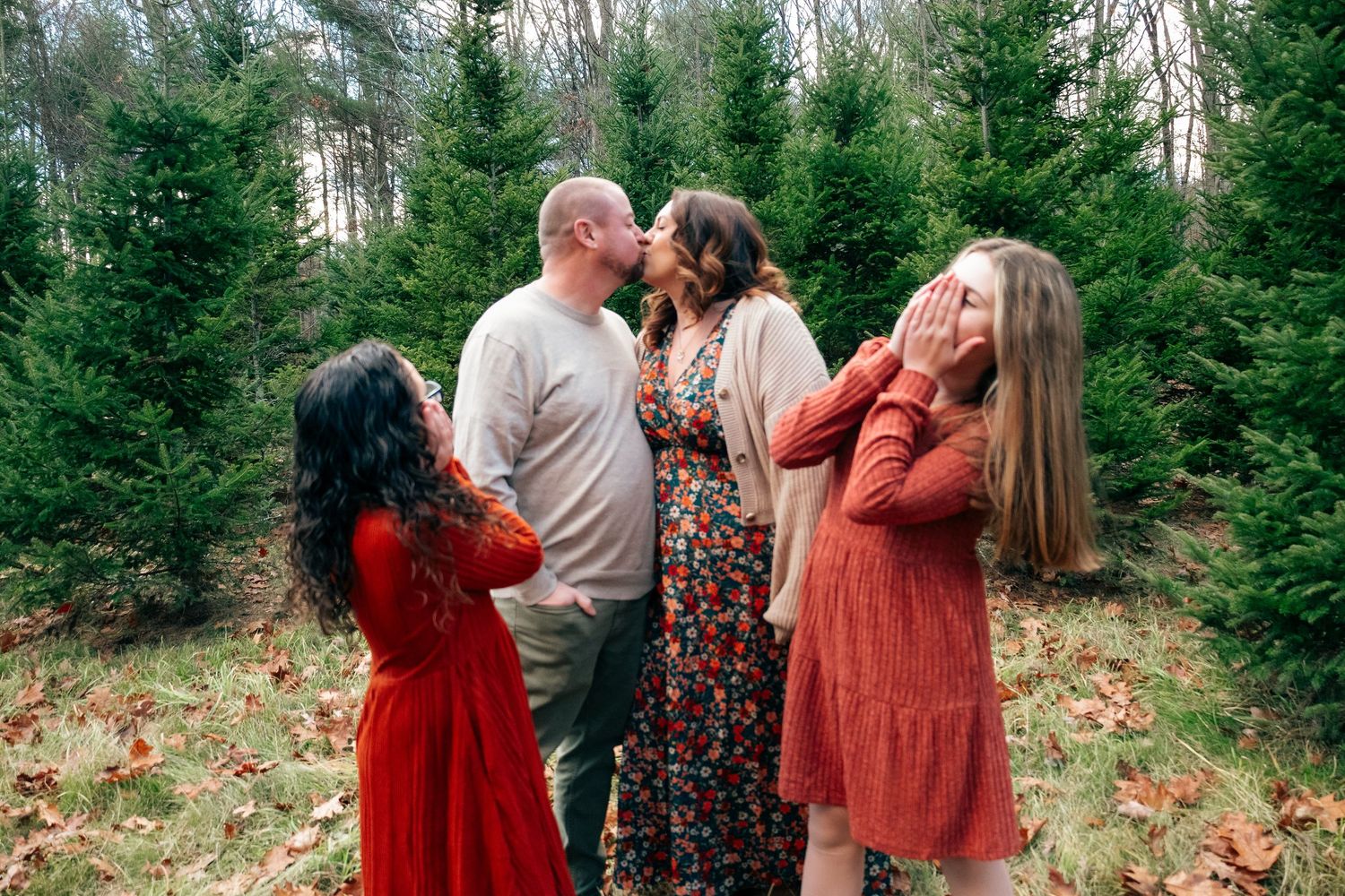 Family photoshoot with multiple people wearing red and neutral tones against a forest backdrop.