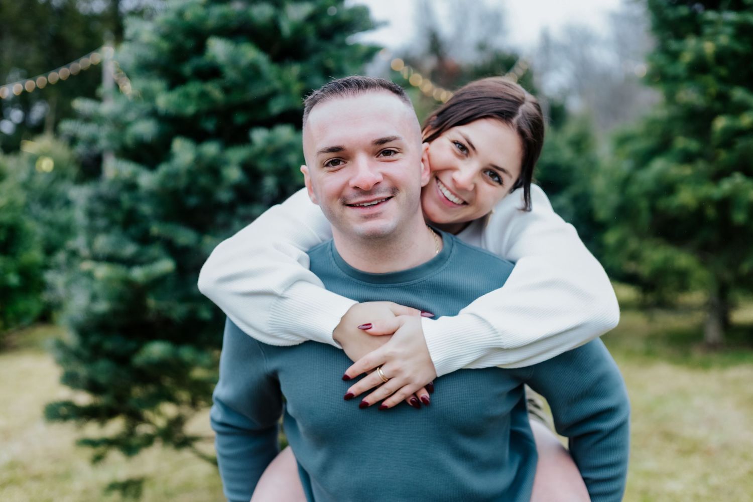 Couple embraces joyfully in a winter outdoor setting with evergreen trees in the background.