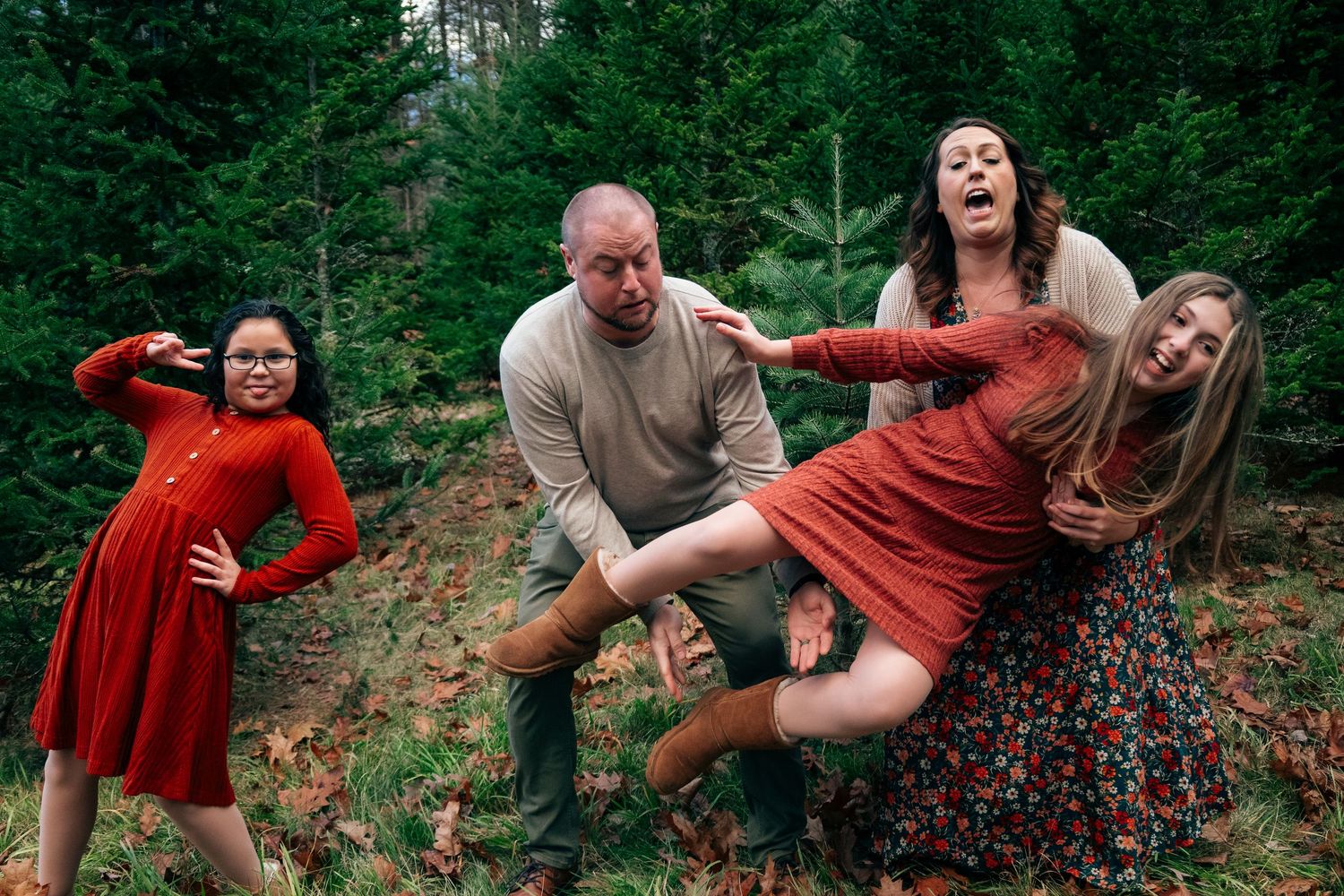 A playful couple poses energetically among evergreen trees during a forest photoshoot.