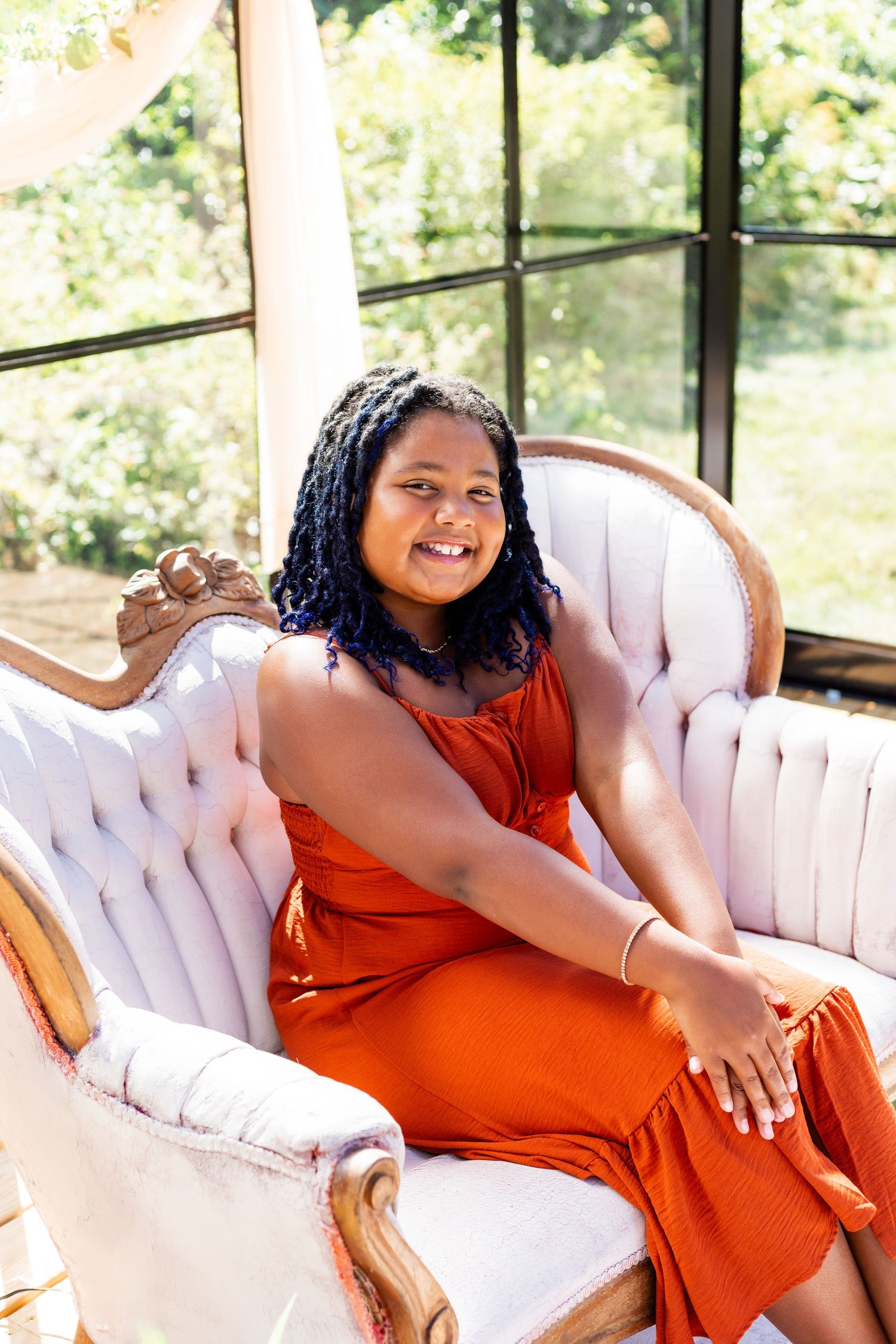 A person in a bright orange dress poses elegantly on a tufted white vintage sofa.