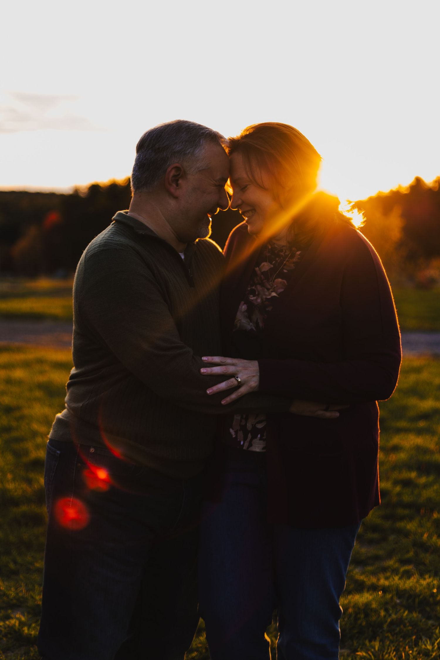 Silhouetted couple sharing an intimate moment at sunset in a grassy field with golden light streaming behind them.