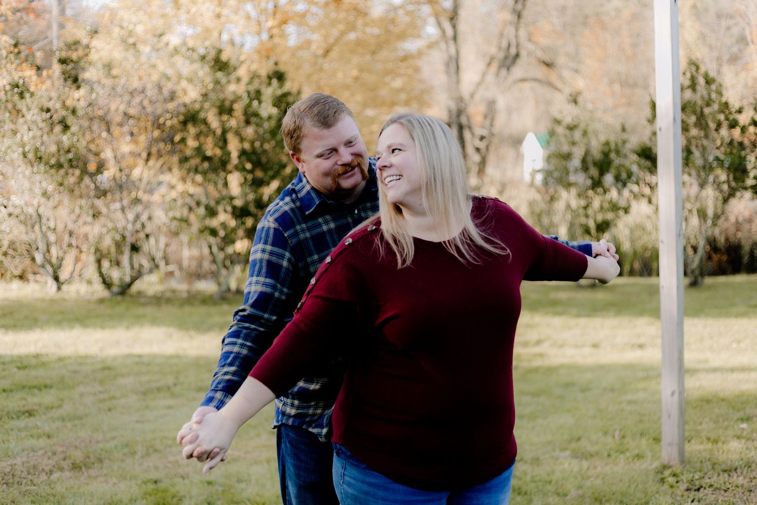 Playful couple laughing and dancing together outdoors near a vintage tractor.