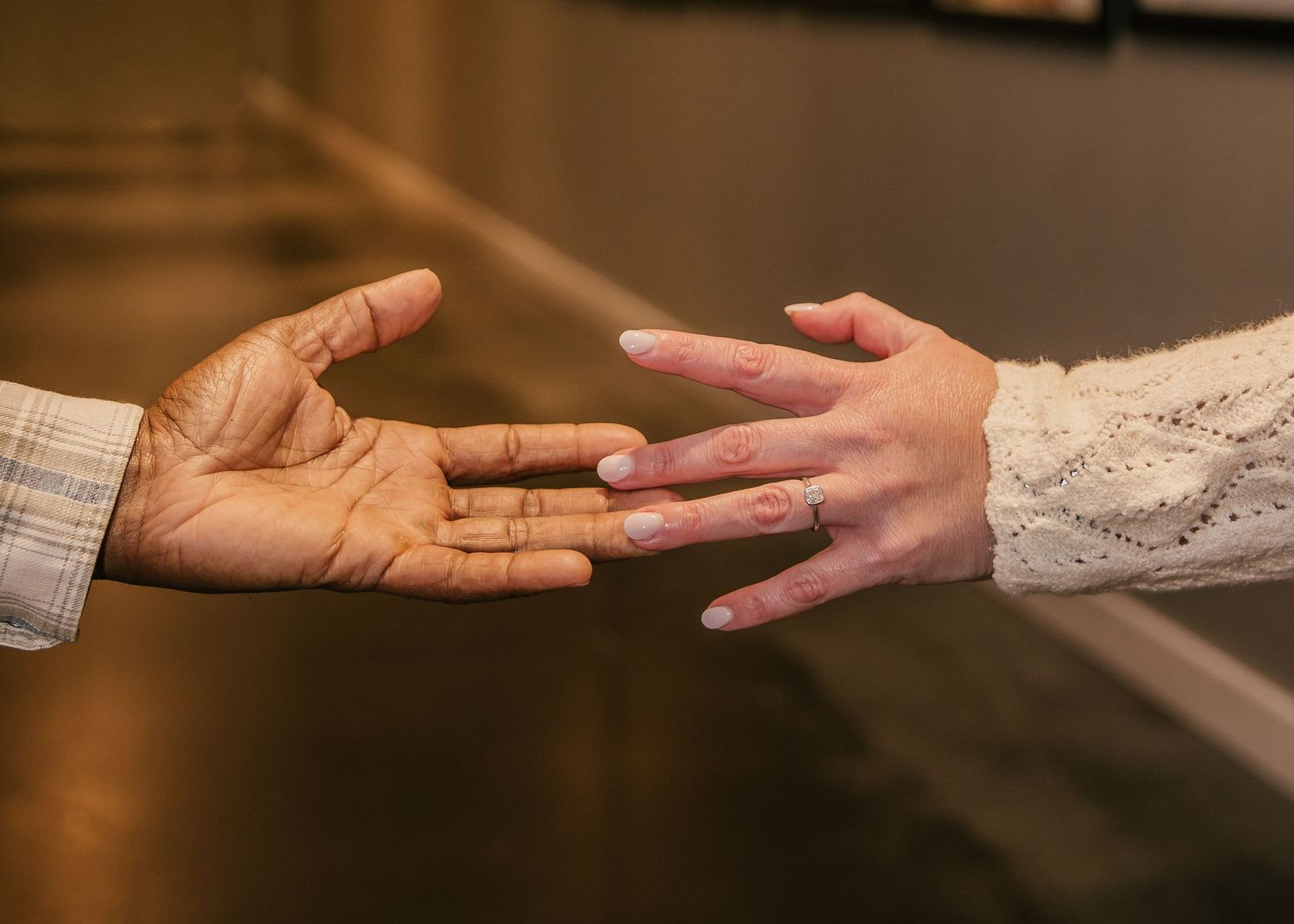 Two hands reaching toward each other in a warm, intimate moment, one in a plaid sleeve and one in a white lace sleeve with a ring.