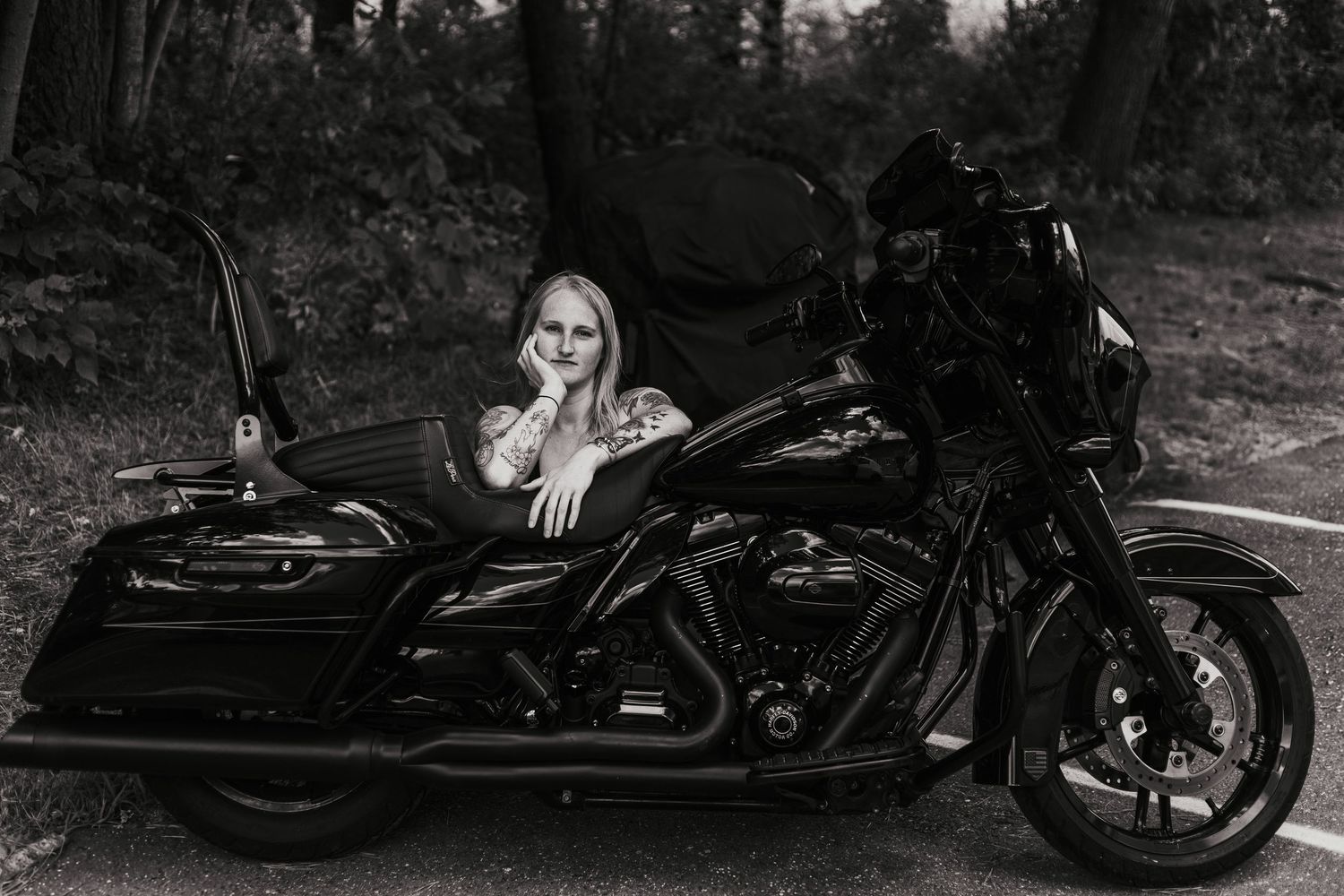 A person poses with a black Harley Davidson motorcycle in a moody black and white photo.