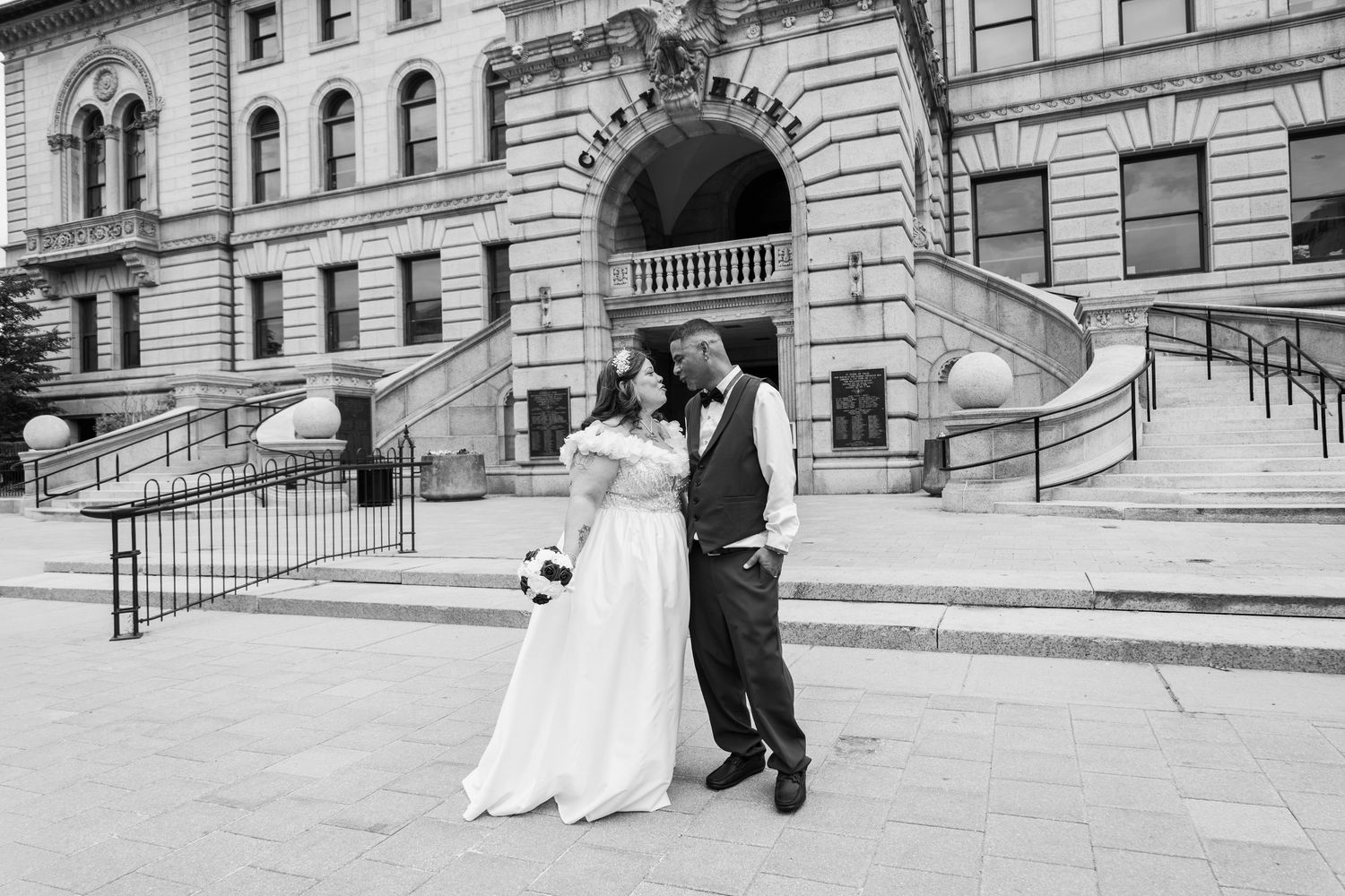 Black and white photo of bride and groom posing in front of a historic city hall building.