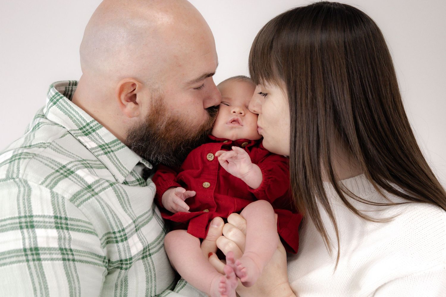 An intimate family portrait in soft lighting with green plaid and red accents.