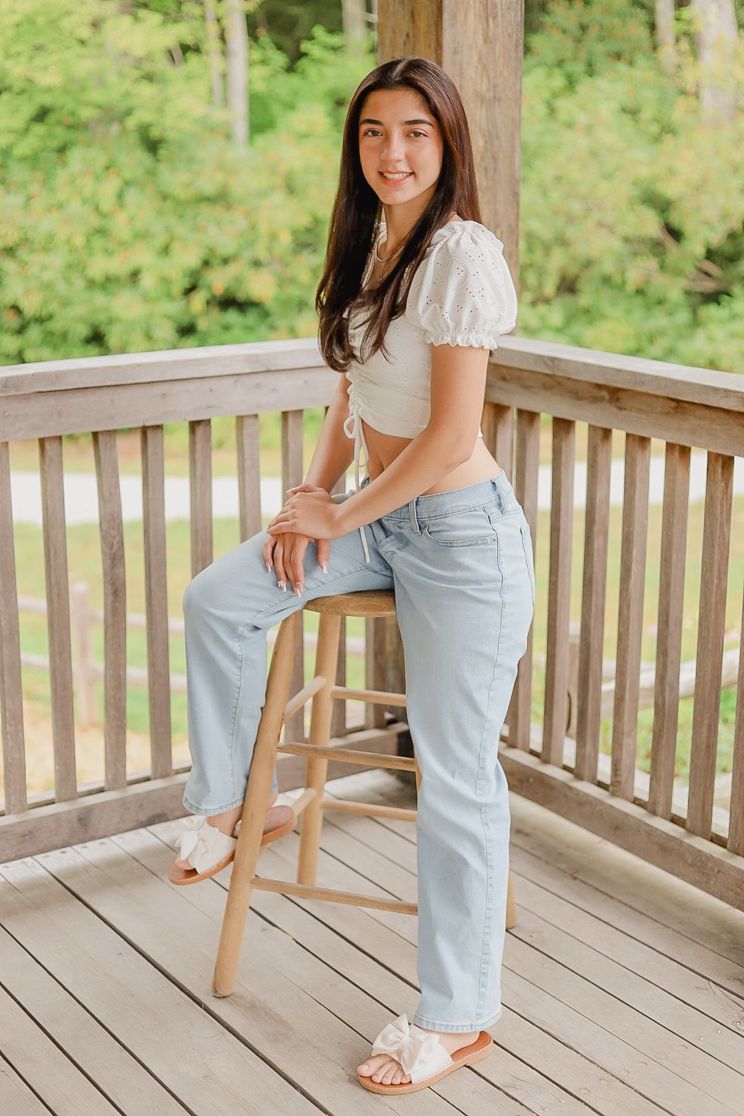 A casual pose on a wooden chair shows off light denim and a white top on an outdoor deck.