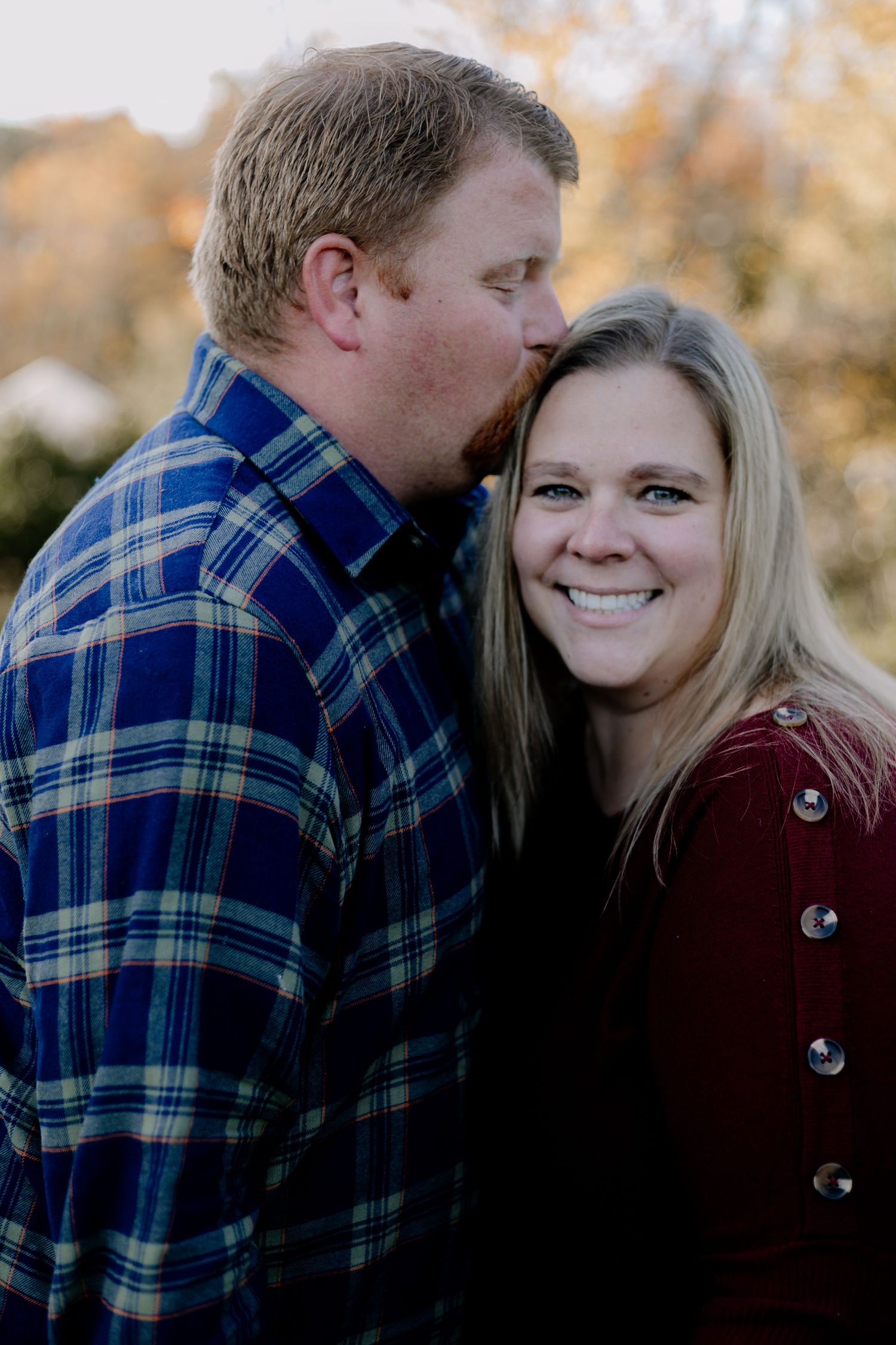 A couple shares intimate moments outdoors wearing plaid and burgundy during an autumn photoshoot.