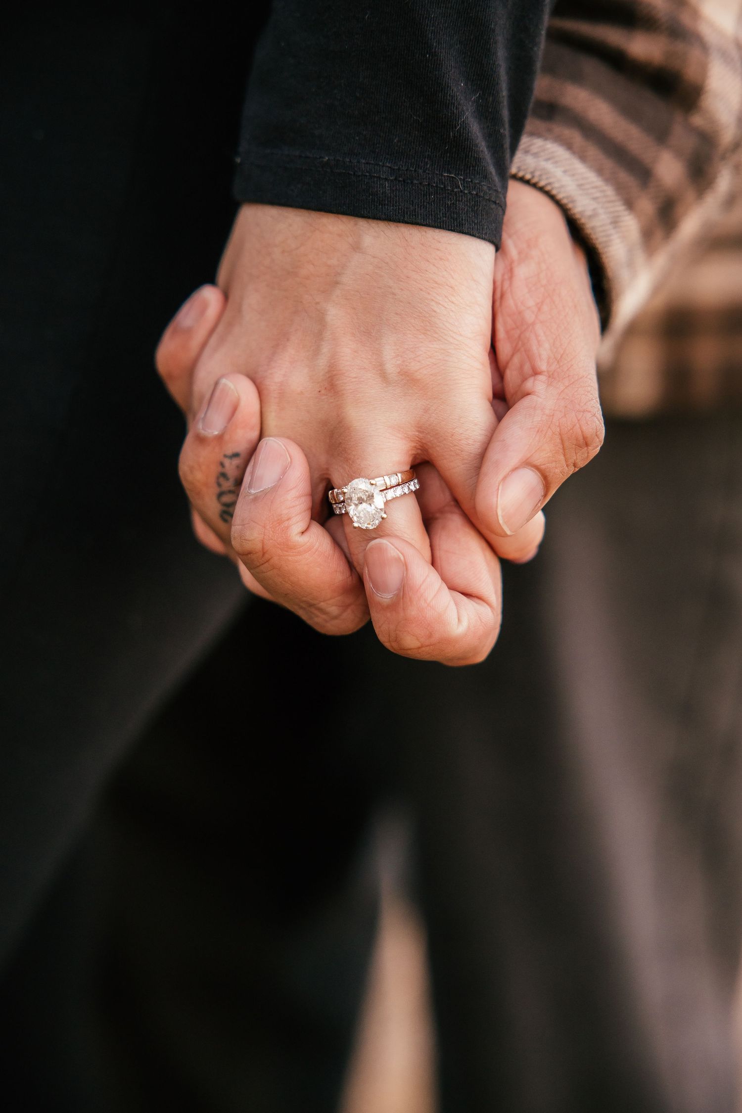 Close-up of two people holding hands, woman wearing a diamond engagement ring and wedding band.