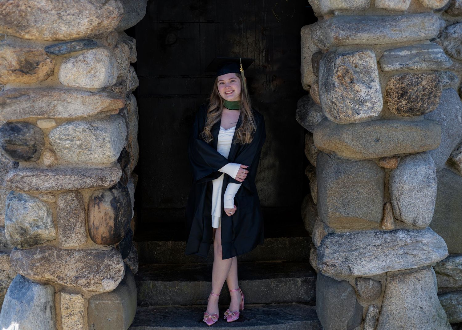 Stone archway frames graduation photo session outdoors.