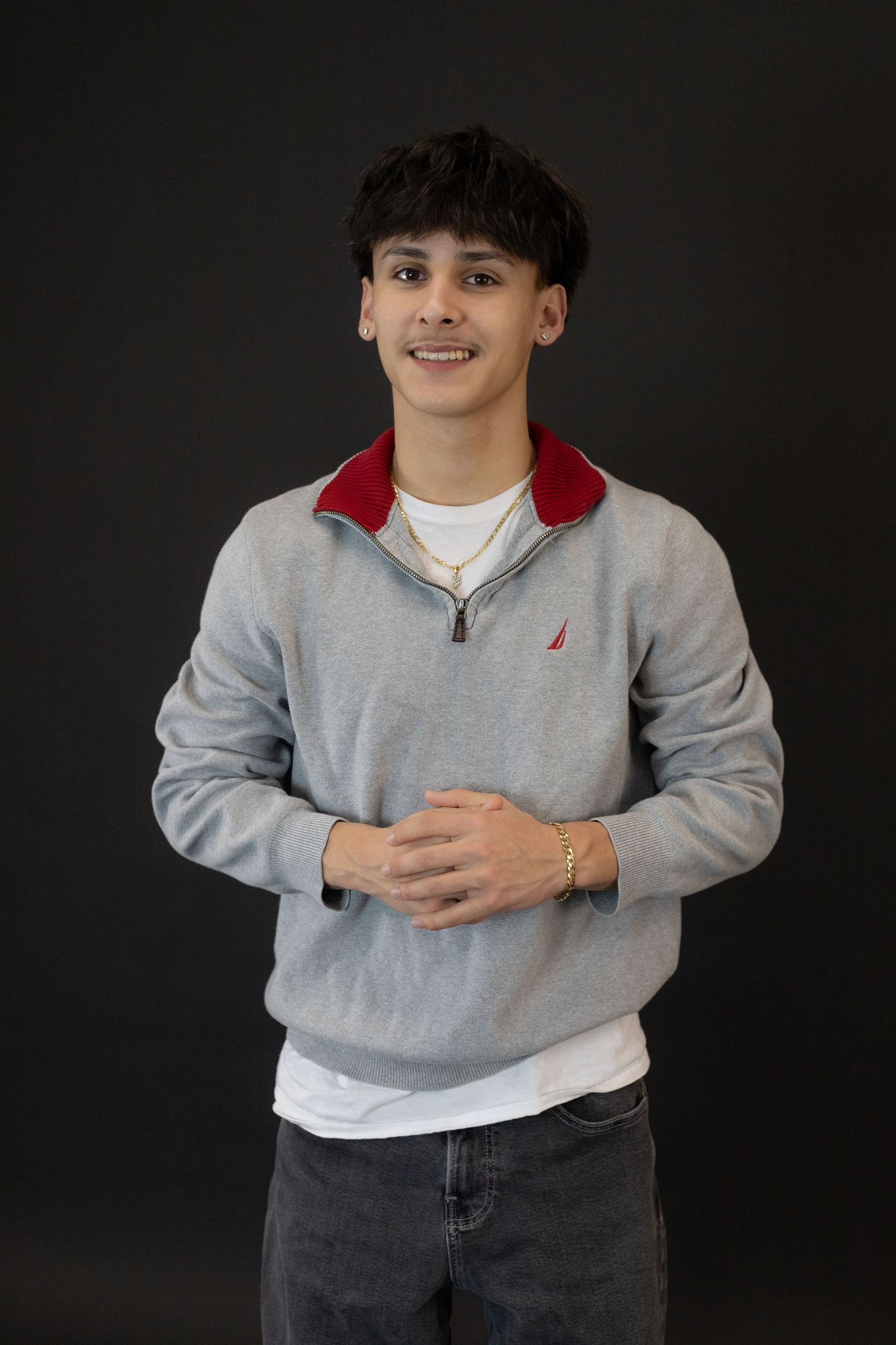 Young man smiling in gray Nautica quarter-zip sweatshirt with red collar, wearing braces and gold bracelet.