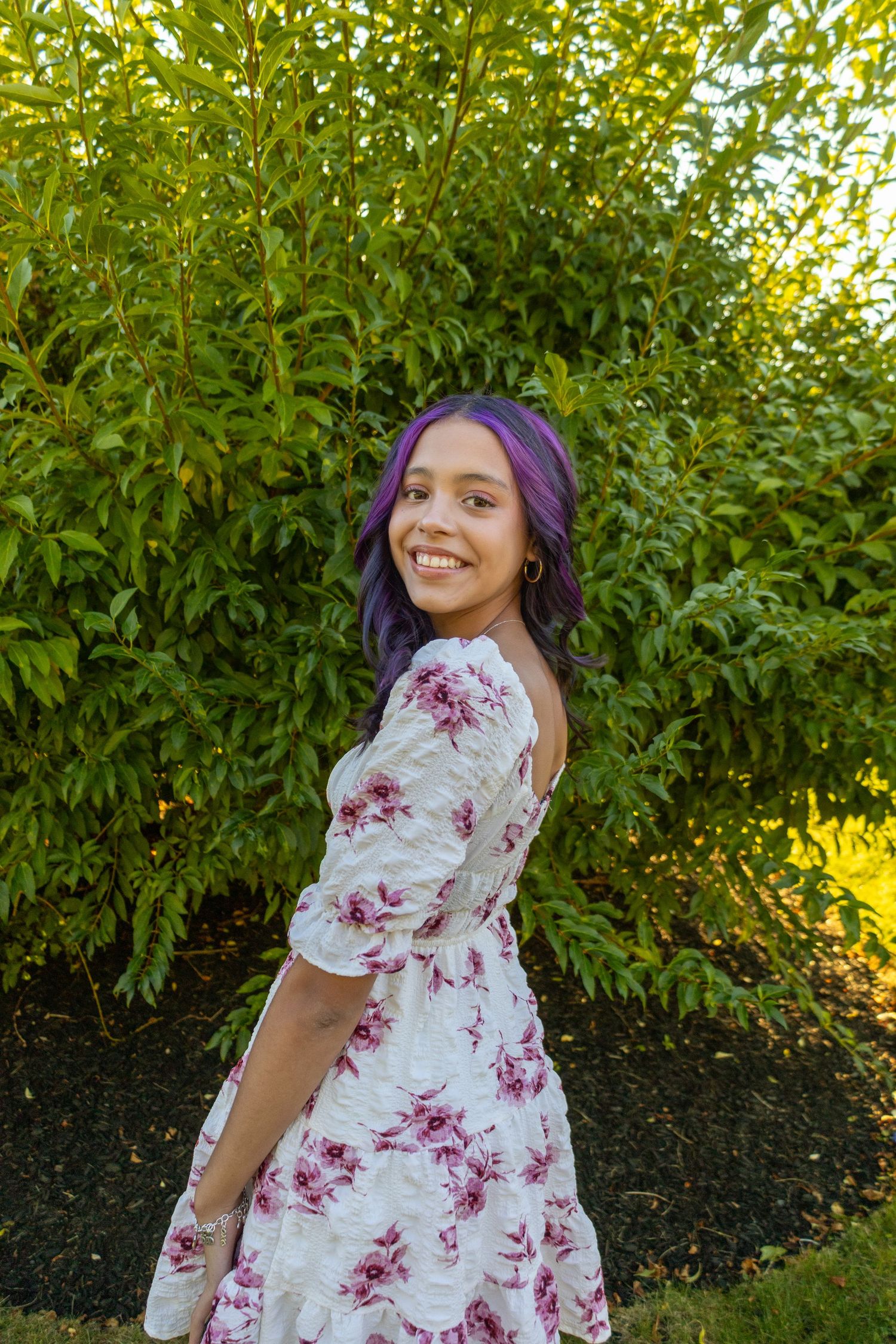 Woman in floral dress poses playfully in garden setting during golden hour.