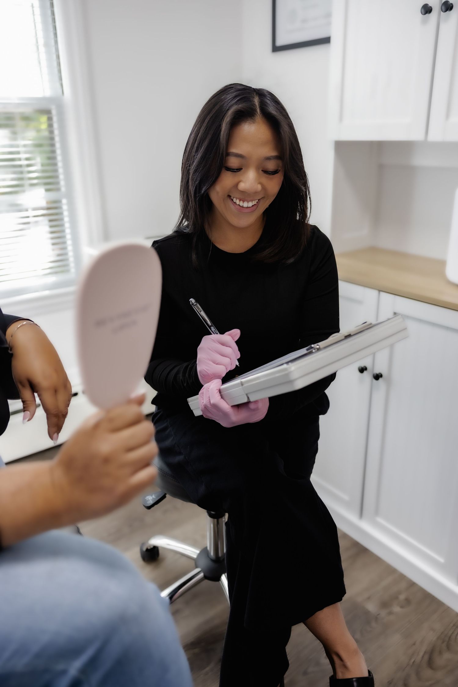 Medical professional in black clothing preparing injection supplies in a bright white clinical setting.