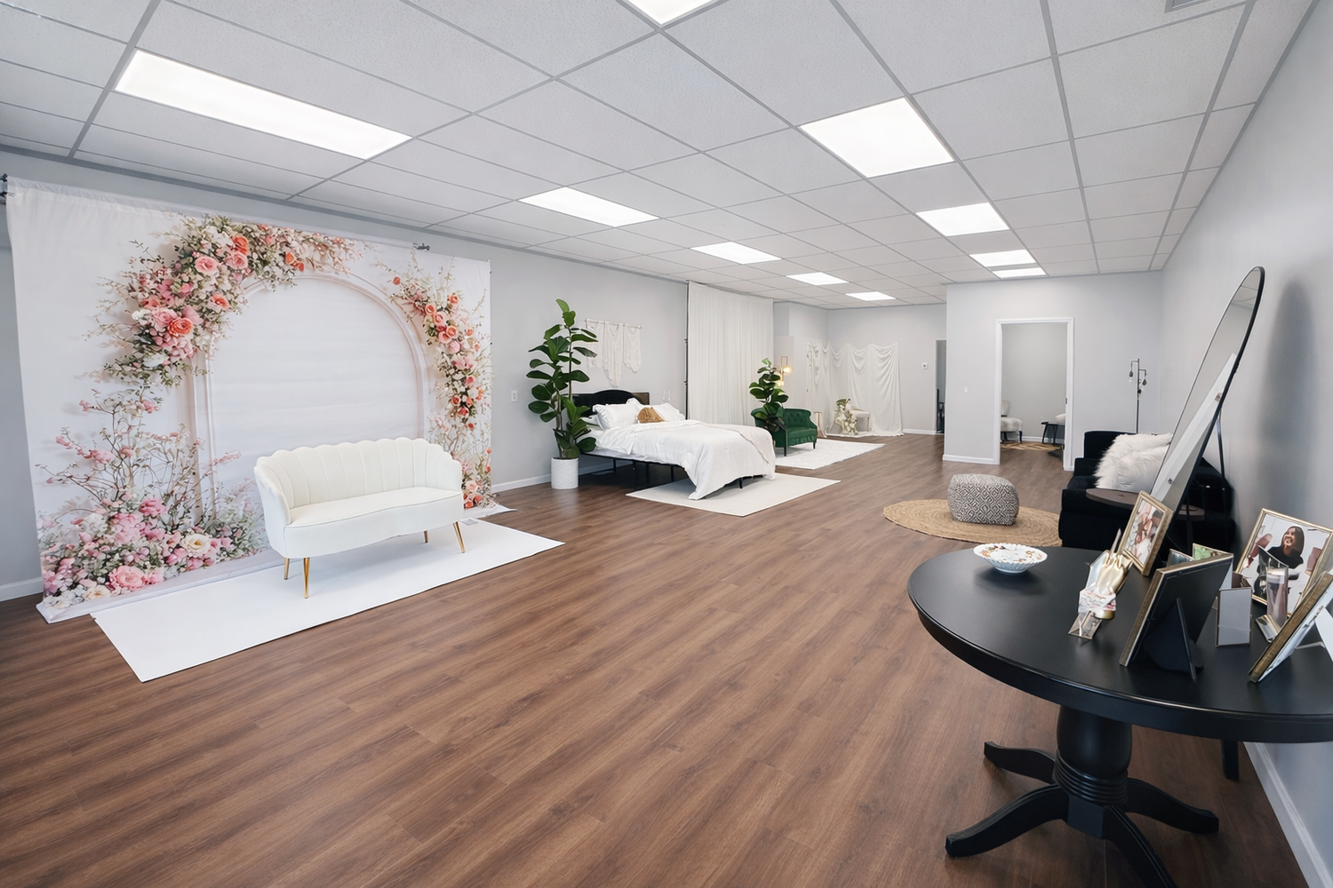 Spacious photography studio with floral arch backdrop, white loveseat, and wood floors.