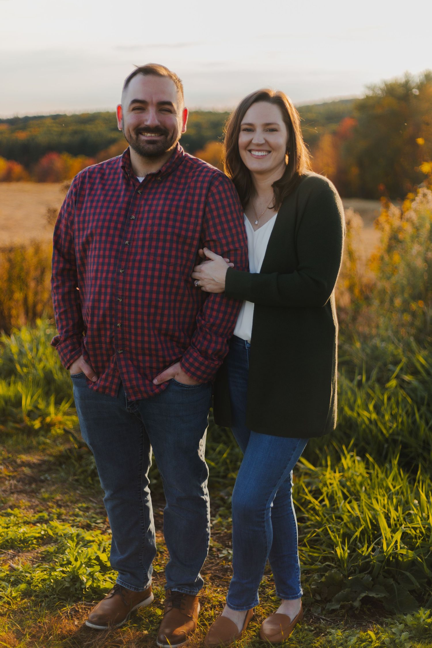 Happy couple smiling together during golden hour in a field with autumn colors in background.