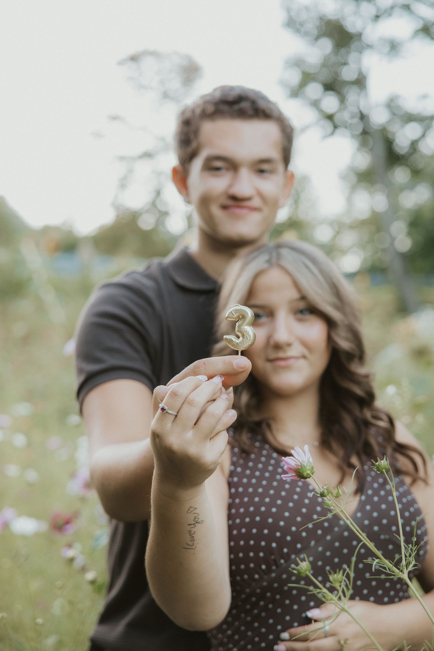 Couple holding a number 3 sparkler in a flower field, celebrating their 3rd anniversary outdoors.
