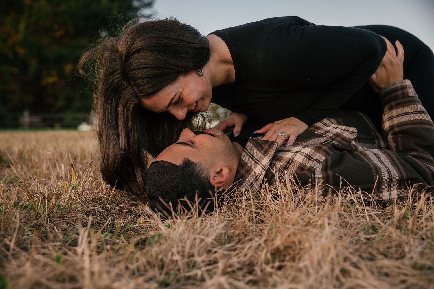 A couple shares a romantic moment in a grassy field, with the woman leaning over the man lying down.