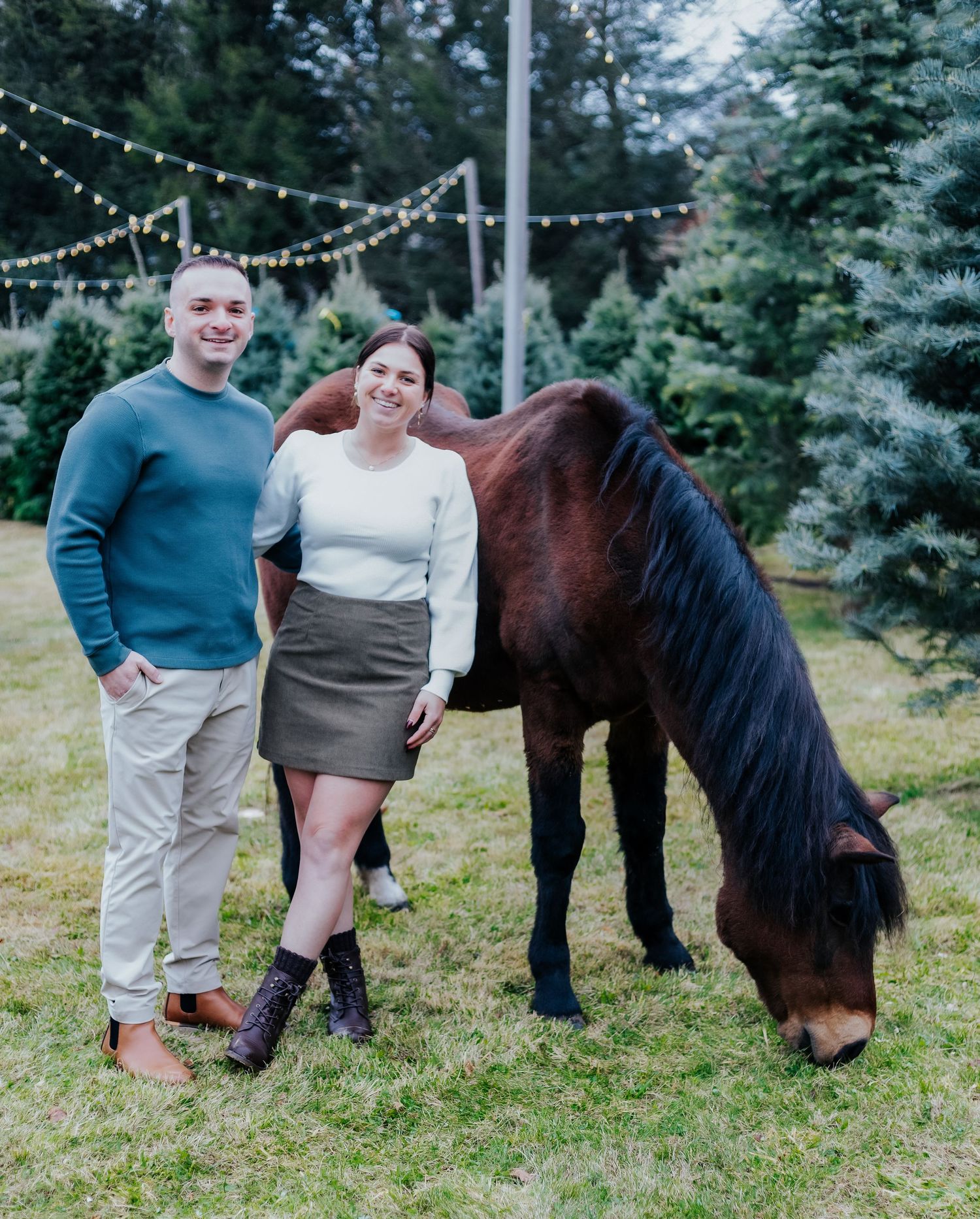 Family poses with a miniature pony in a festive outdoor setting with string lights.