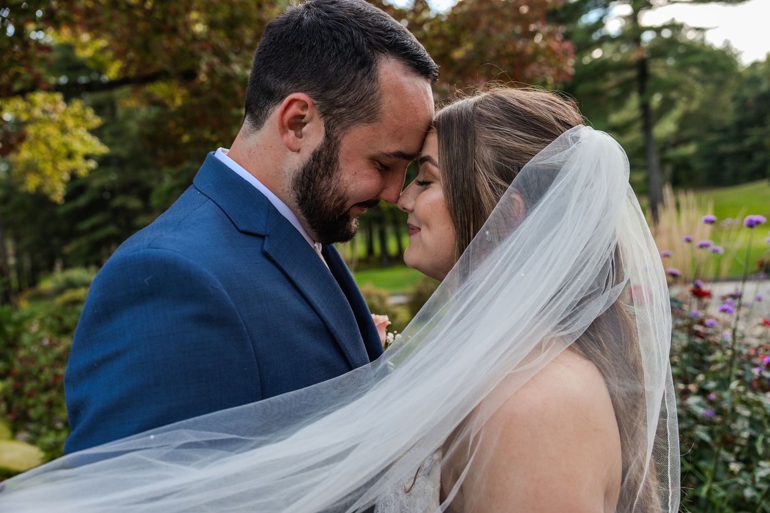 Romantic couple embrace in garden setting during wedding photoshoot.