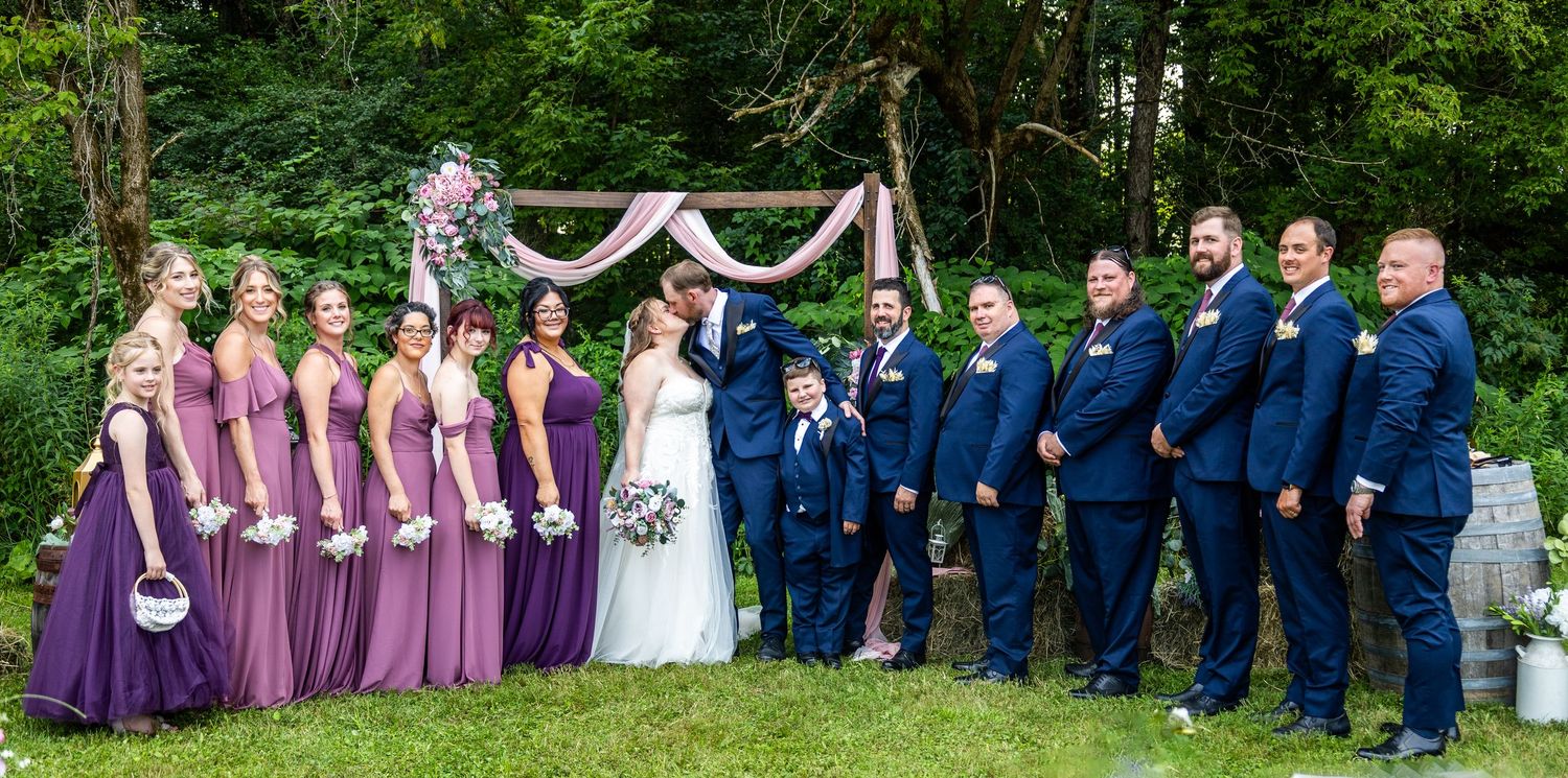 Wedding party in purple and navy formal attire posing outdoors.