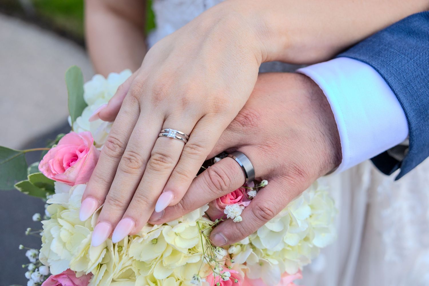 Close-up of wedding rings and hands with pink and white floral details.