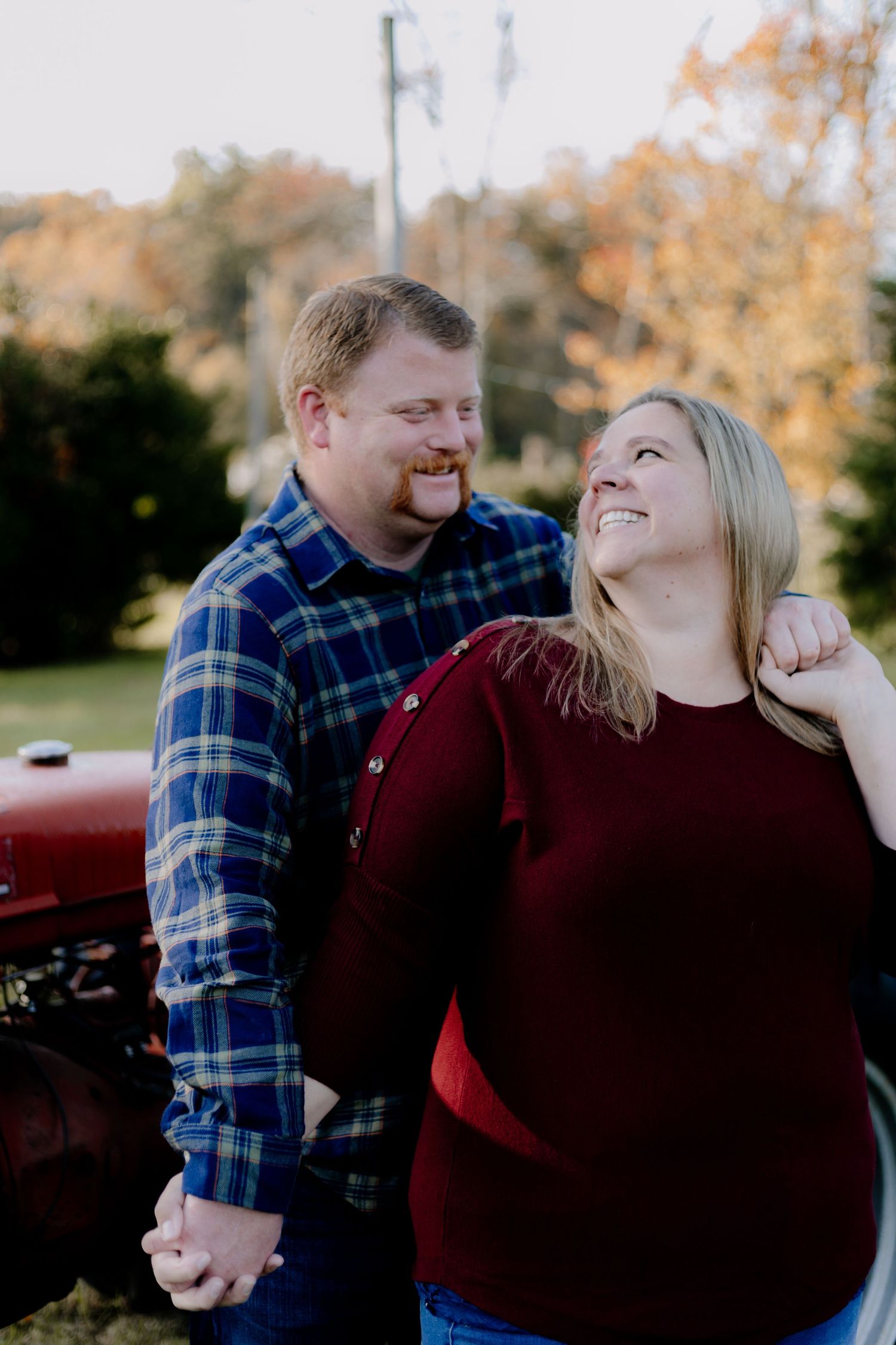 A couple laughs together during a romantic outdoor photo session wearing plaid and burgundy.