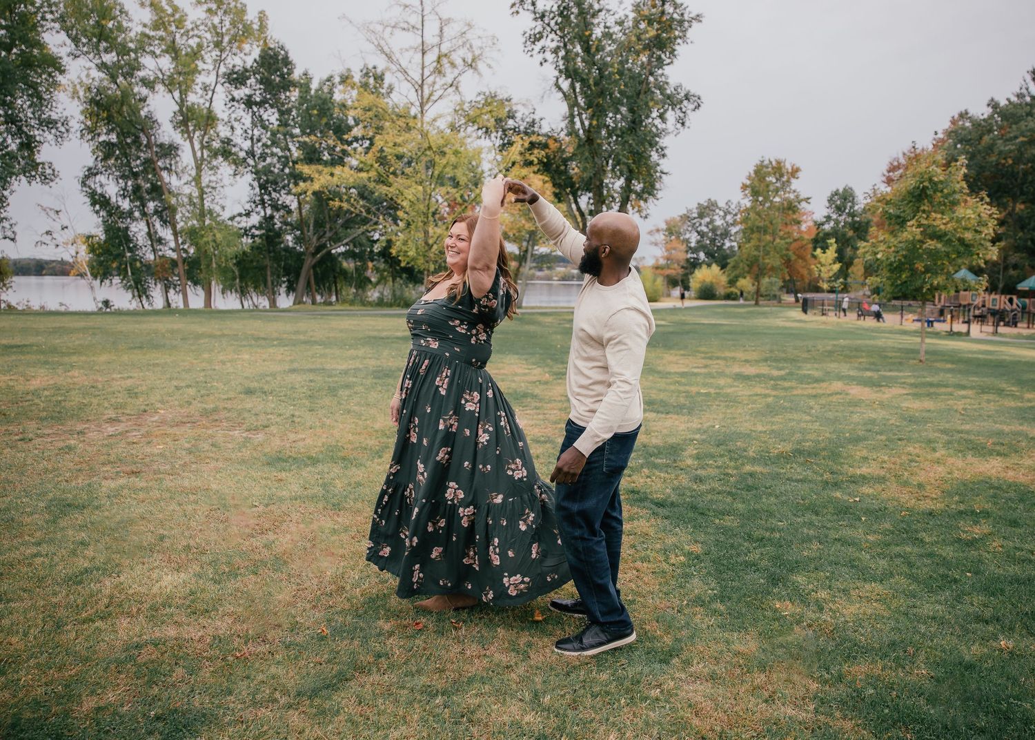 Couple dancing outdoors in a green park, woman in floral dress being twirled by man in white shirt.