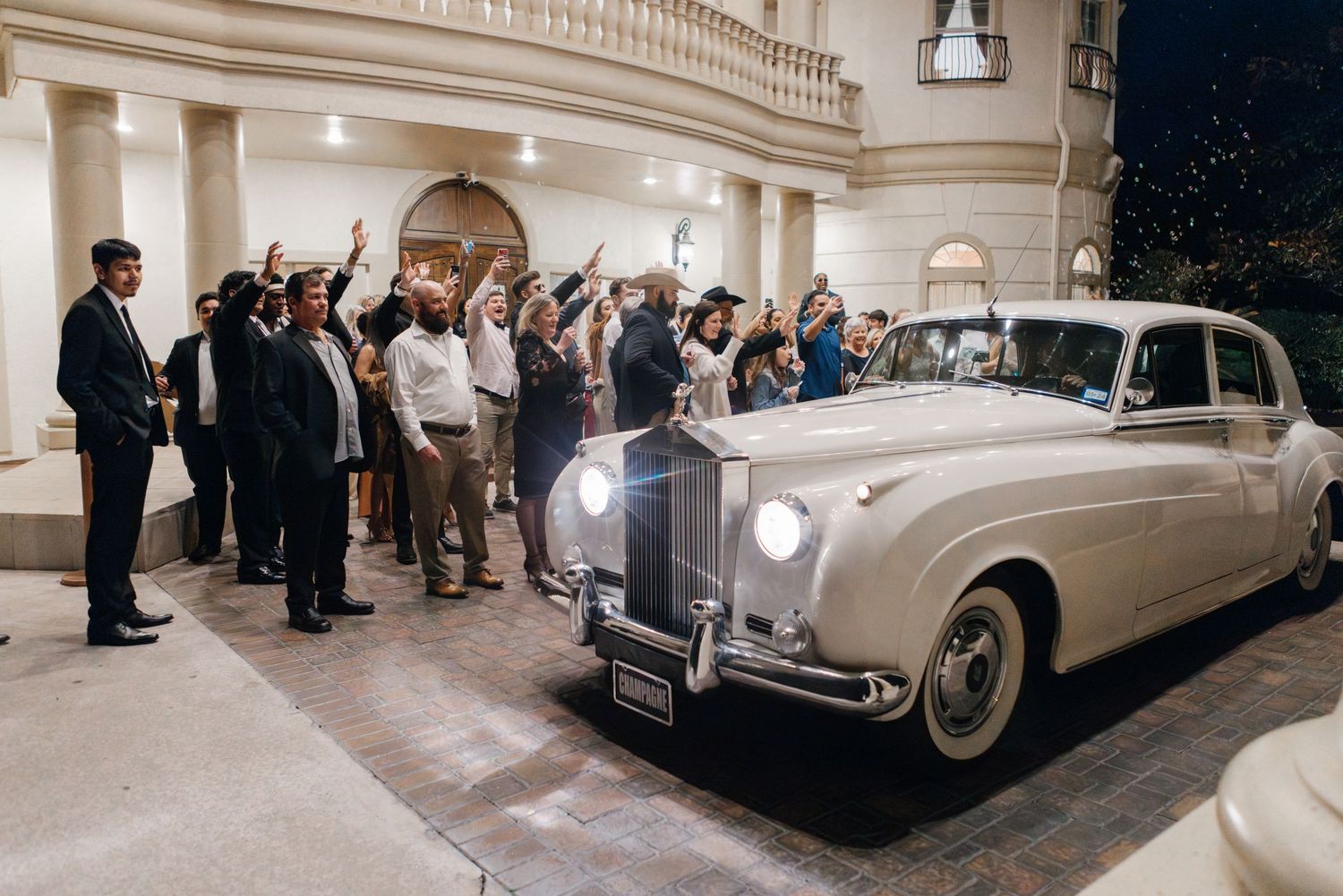 Classic white Rolls Royce with wedding guests gathered outside grand columned building.