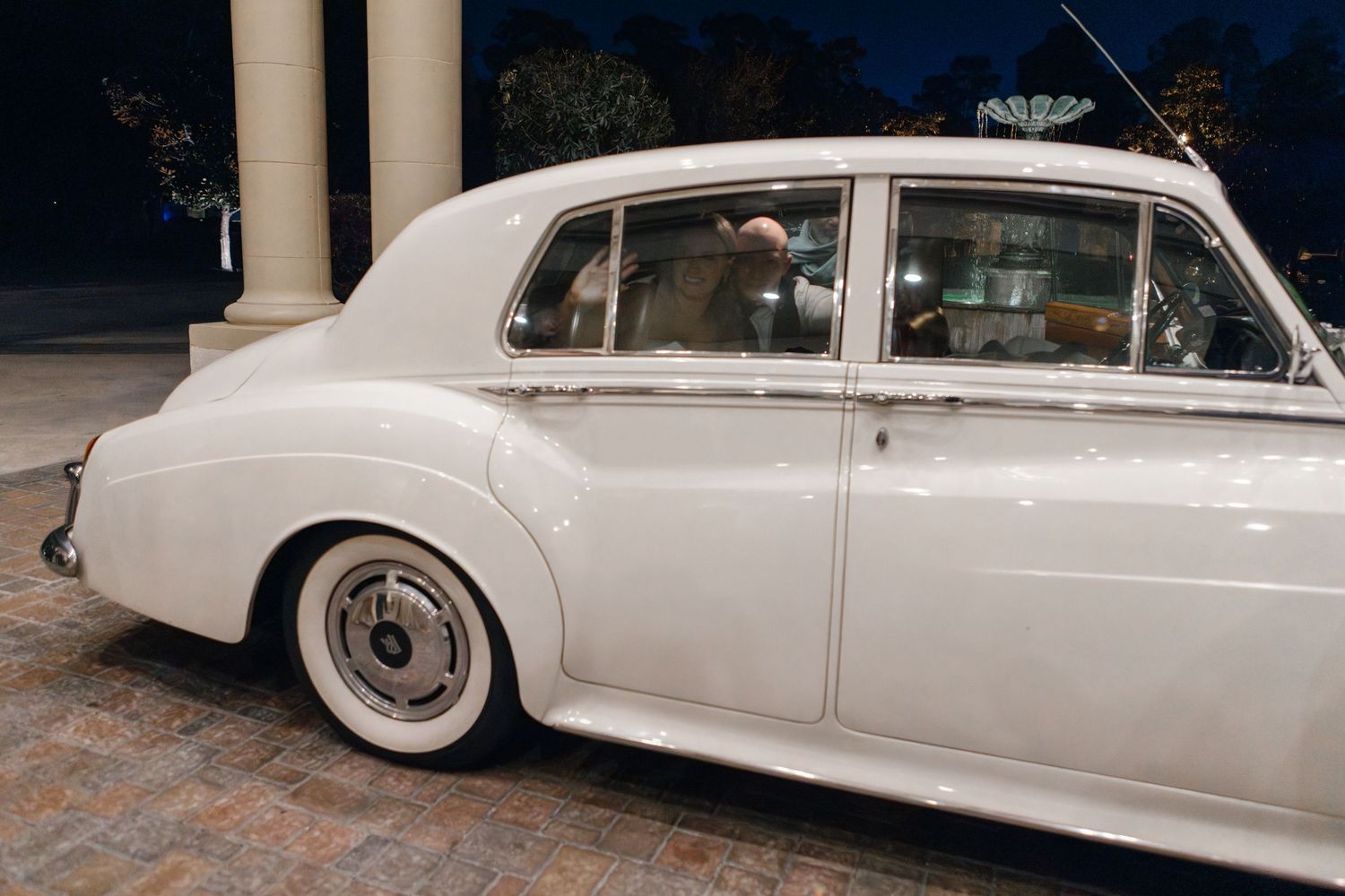 Elegant white vintage Rolls Royce parked on brick pavers.