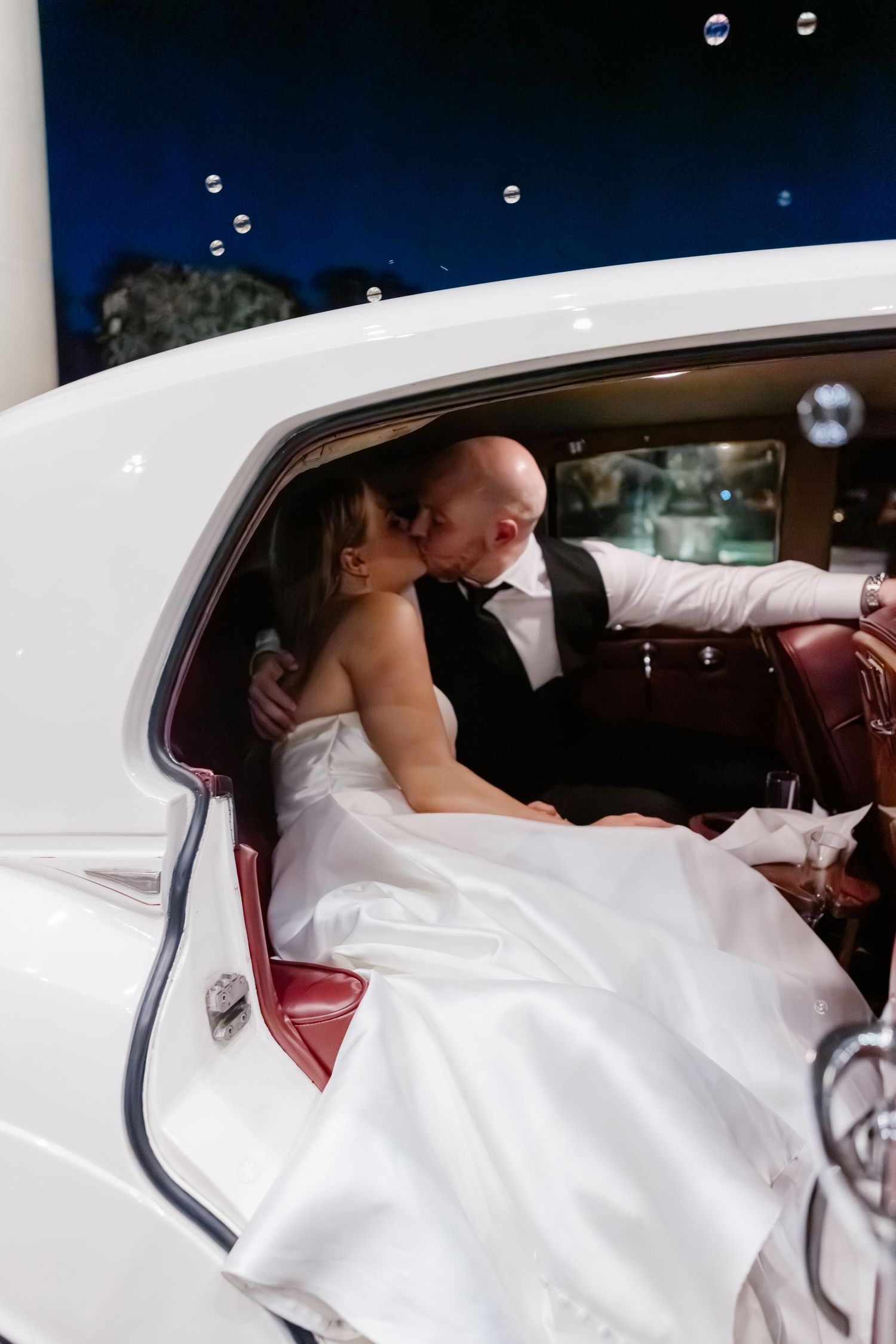 Romantic moment in classic white vintage car during wedding celebration.