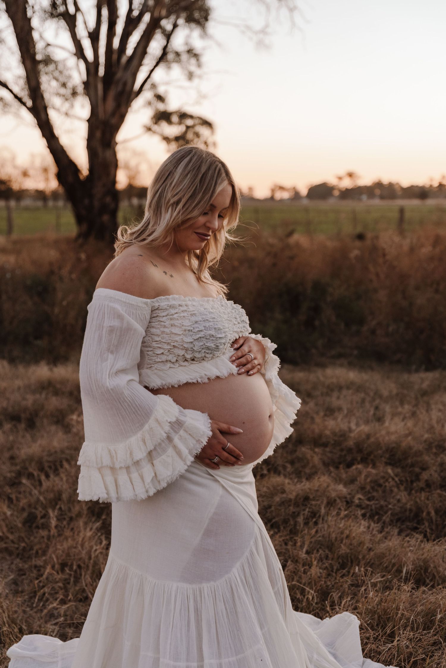 pregnant-mother-embrassing-bump-standing-in-sunset-field-tongala