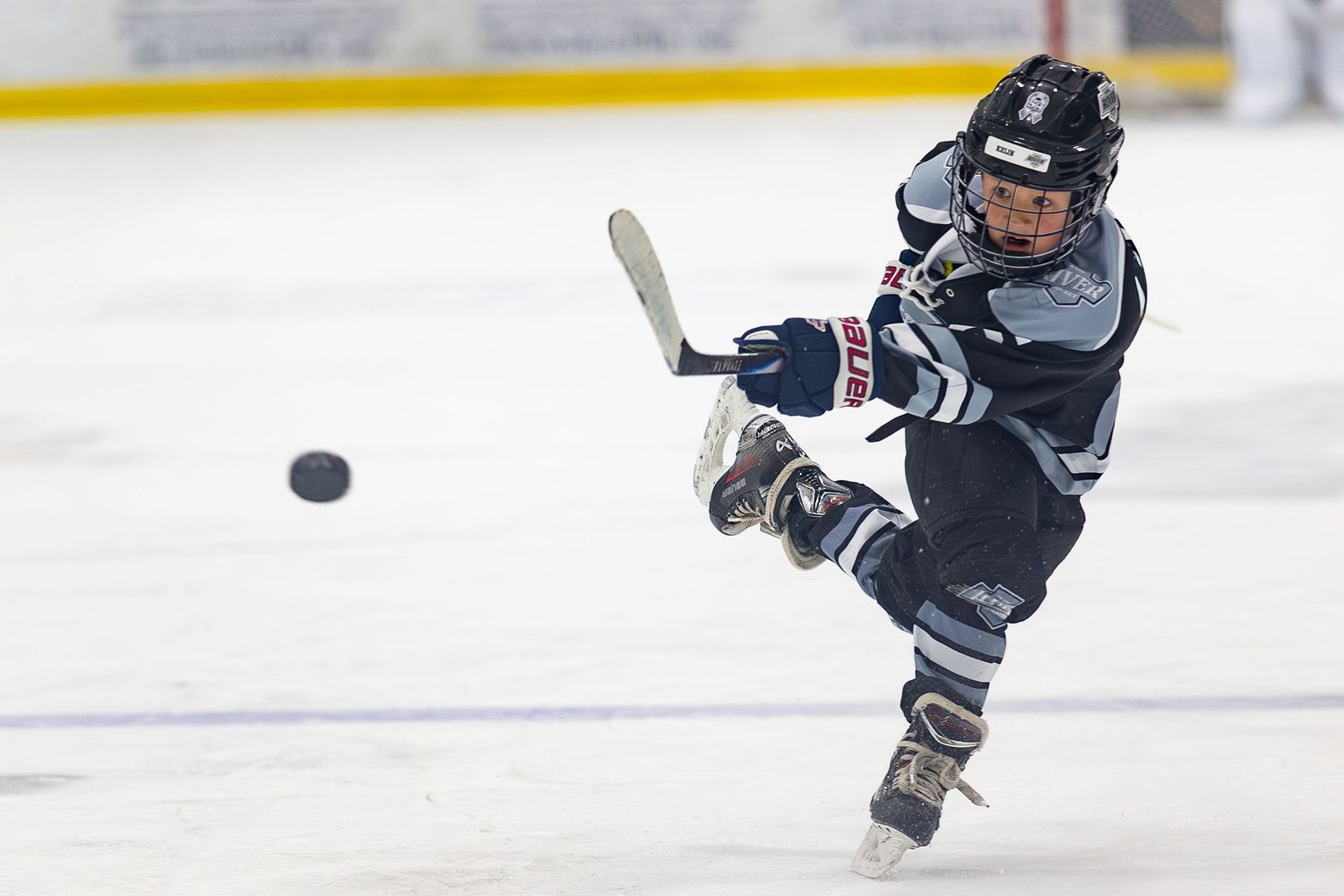 Young hockey player in navy uniform taking a powerful shot on ice.