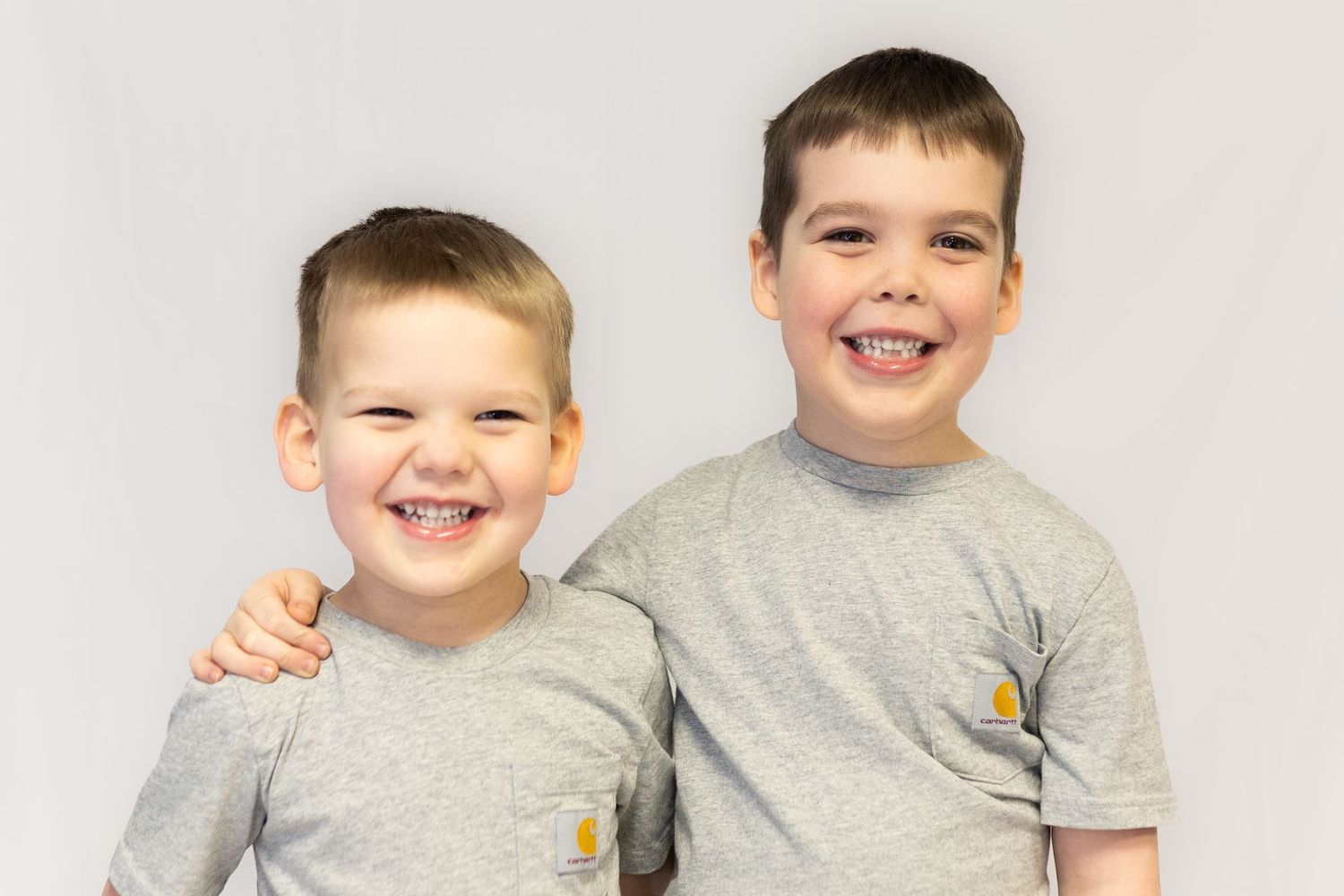 Two smiling brothers in matching grey Carhartt t-shirts posing for portrait photo.