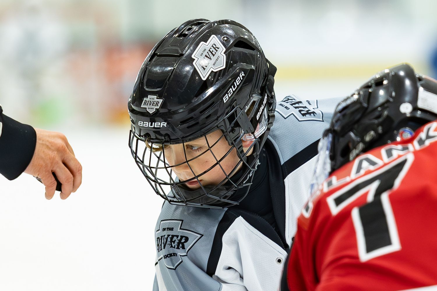 Young hockey player in black River helmet smiling during game on ice rink.